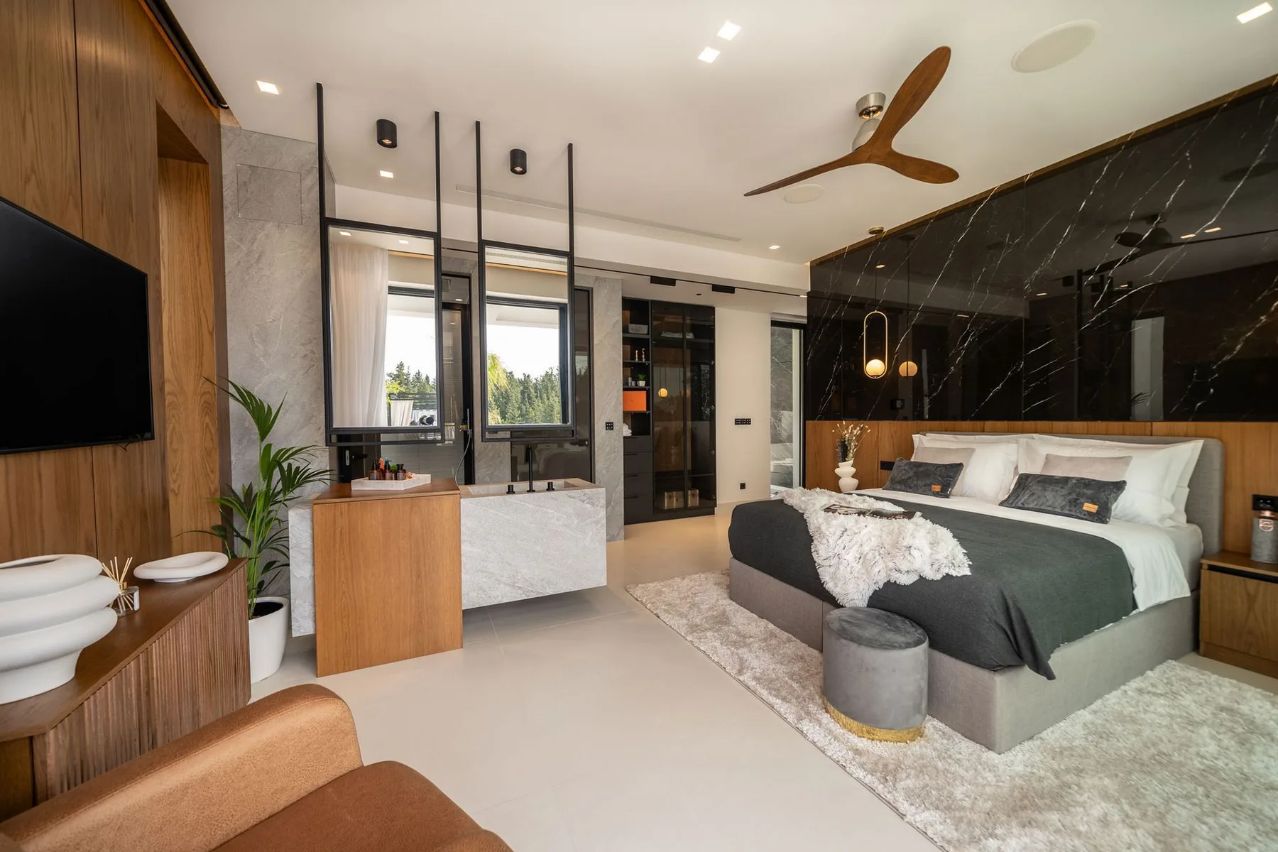 A modern bedroom features a king bed, dark marble accent wall, ceiling fan, and wood-paneled television wall.