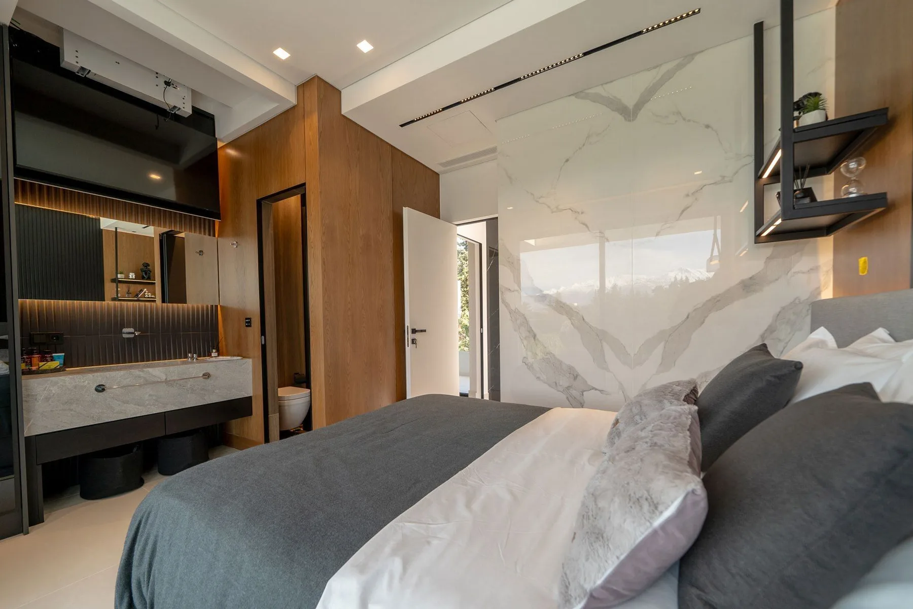 Modern bedroom with a gray bed, marble-patterned wall, and vanity beside the open doorway.