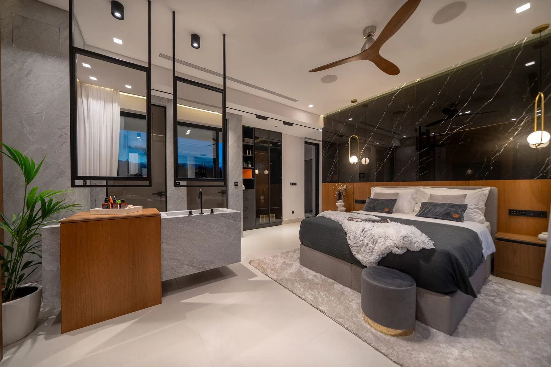 A modern bedroom with a king bed, dark marble accent wall, and a long double-sink vanity.
