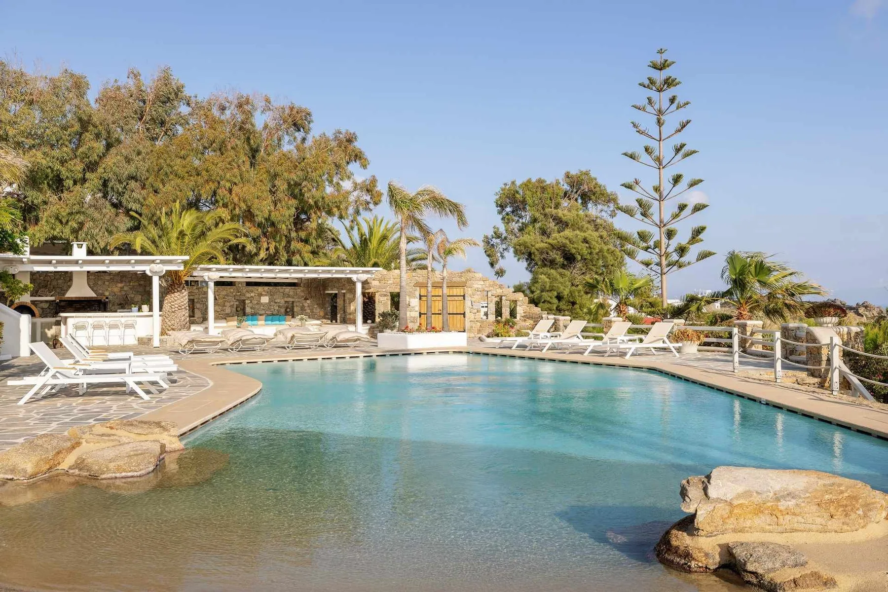 An outdoor swimming pool is surrounded by lounge seating and greenery.