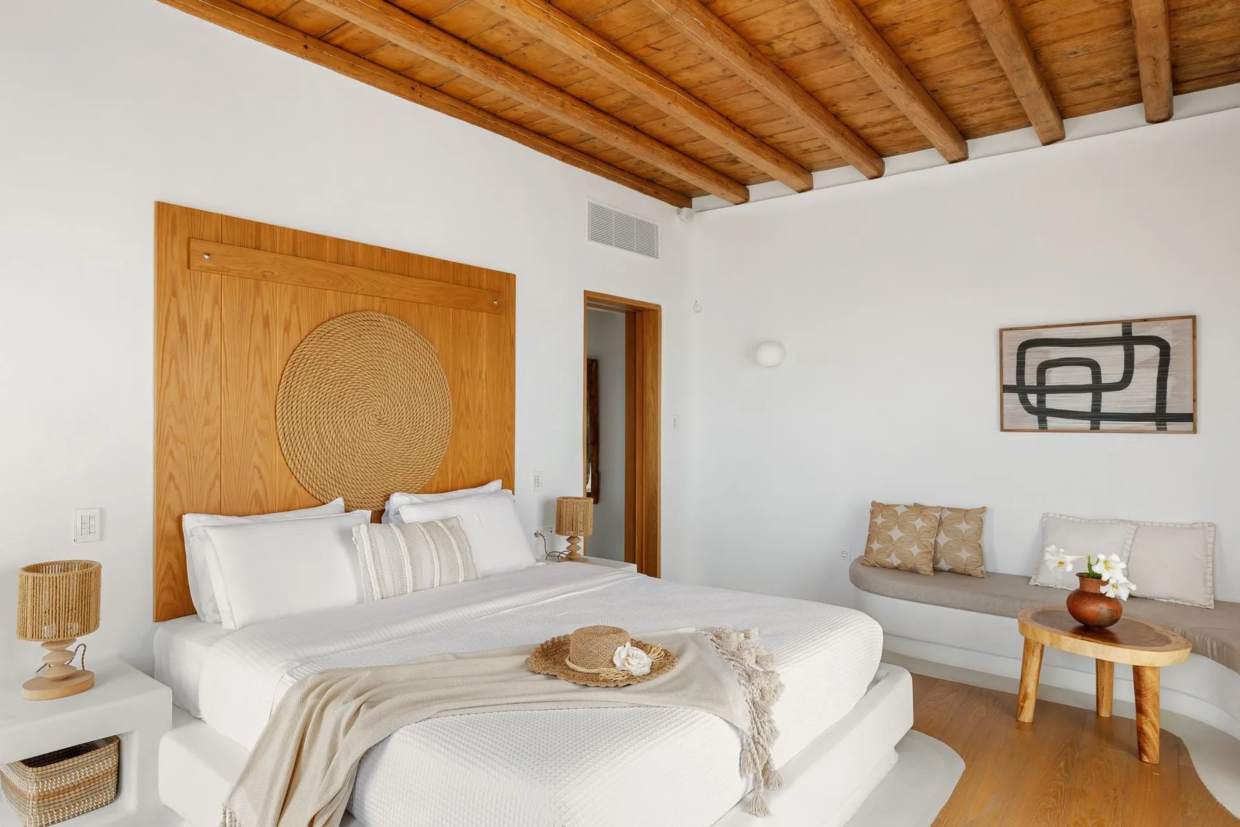 A bedroom with a bed, a small seating area, and a wooden ceiling.