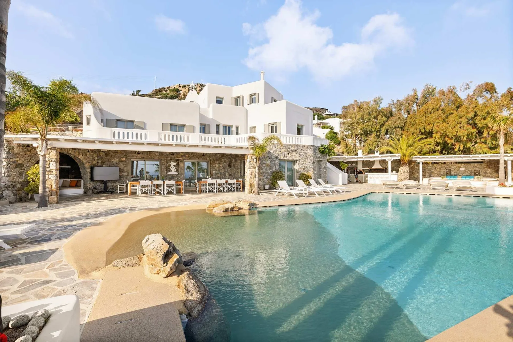 Outdoor pool beside a white building, with a stone patio and lounge seating.