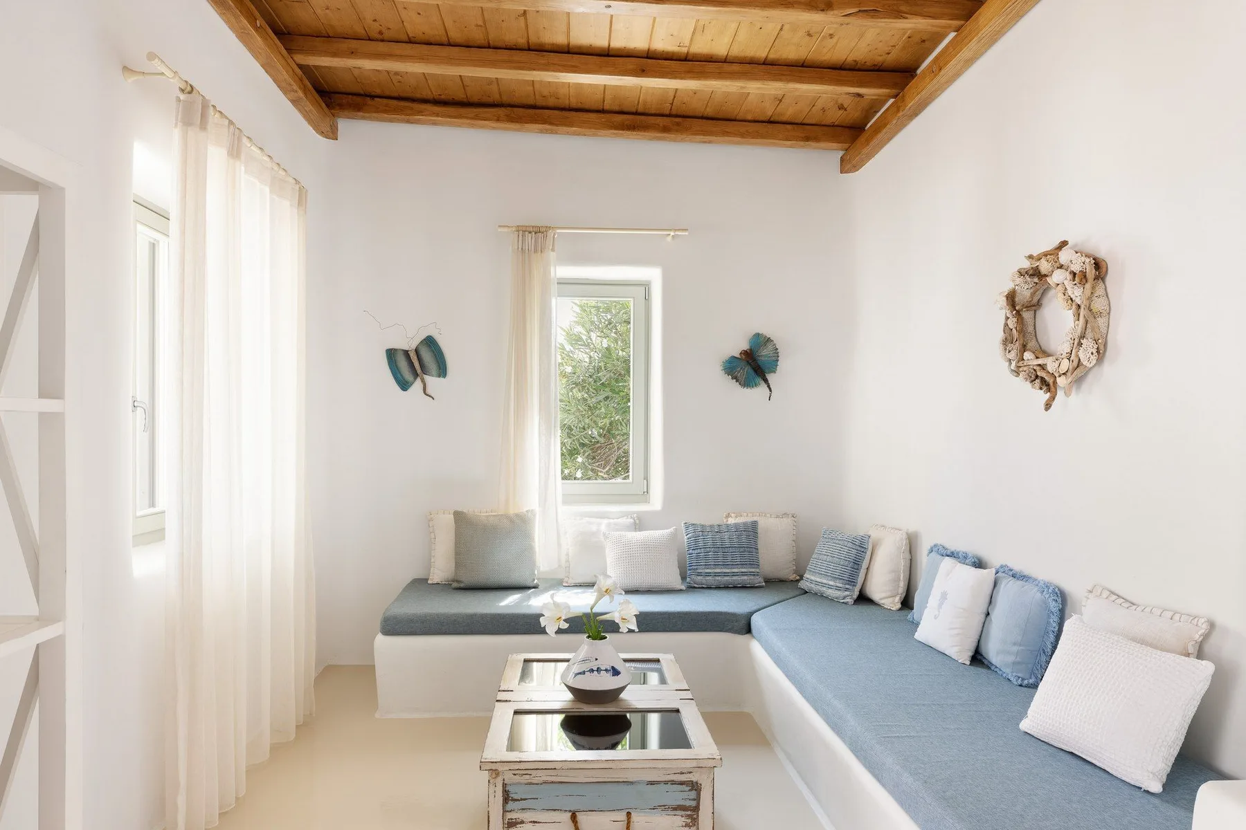 A bright living room with an L-shaped seating area and exposed wooden ceiling beams.
