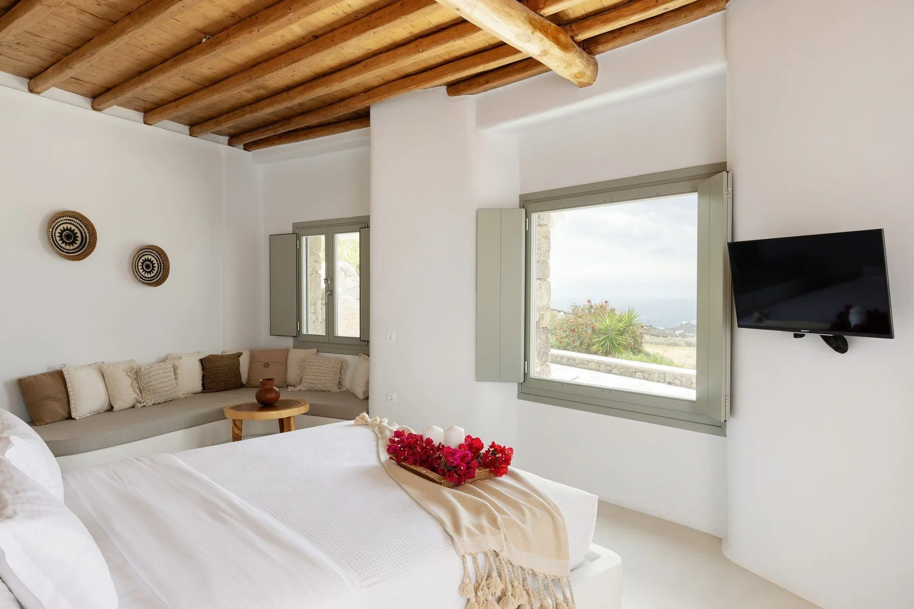 Bedroom with a bed, corner seating, and a wall-mounted television.