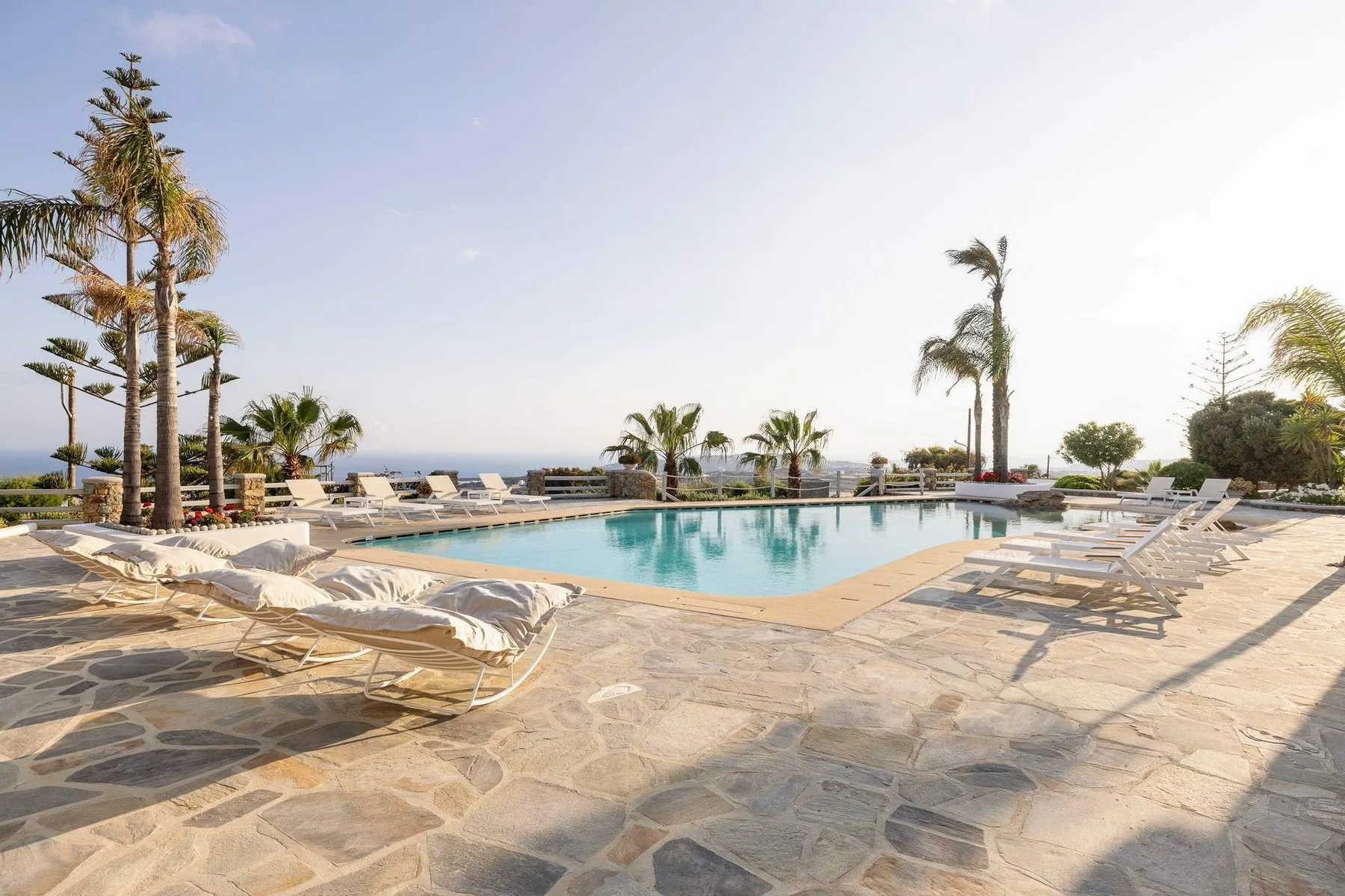 An outdoor swimming pool is surrounded by lounge seating and palm trees.