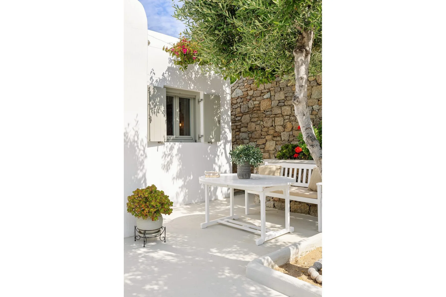 A shaded outdoor patio with a white table and seating beside a stone wall.