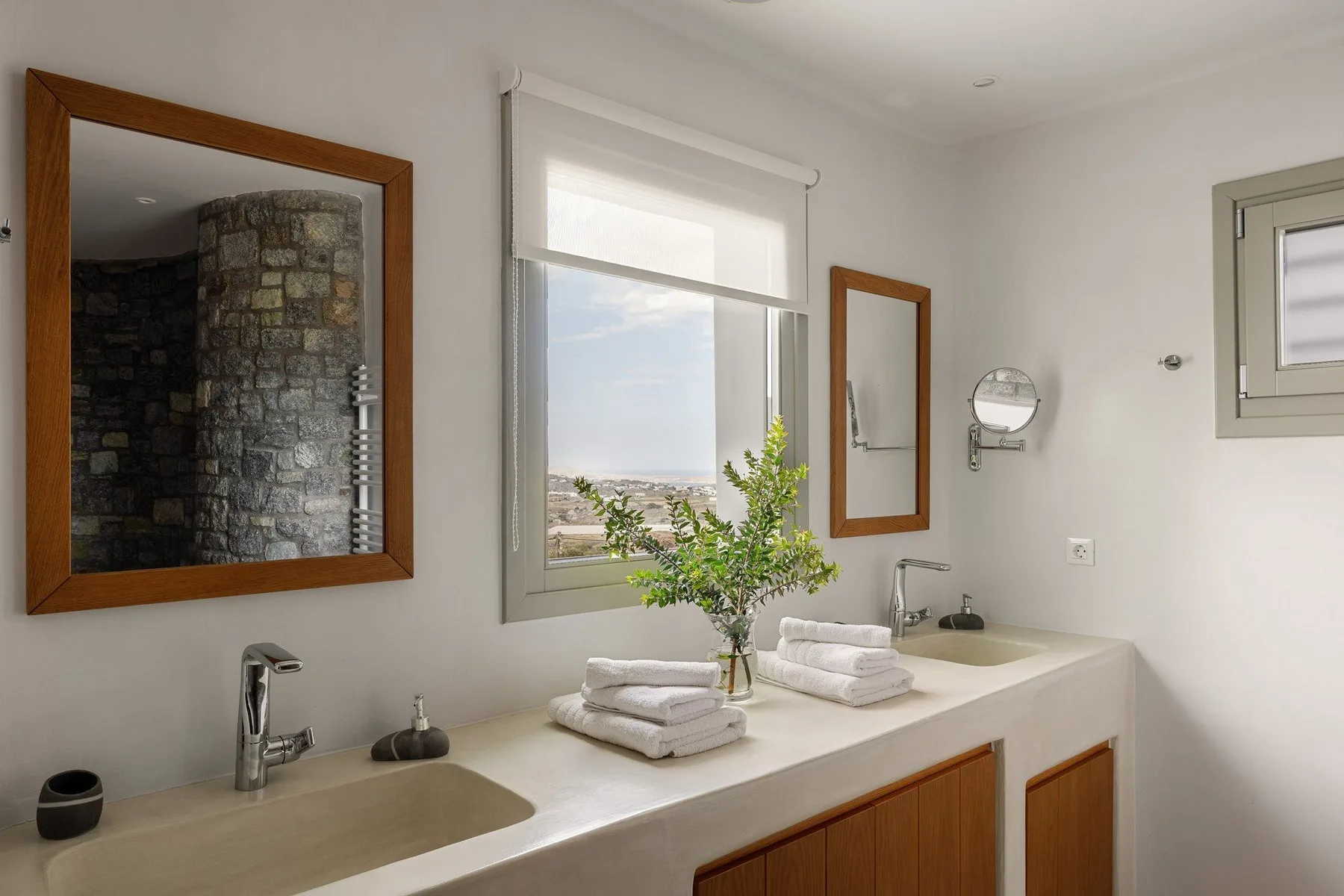 A bright bathroom with a wide counter, sinks, and a window overlooking the landscape.