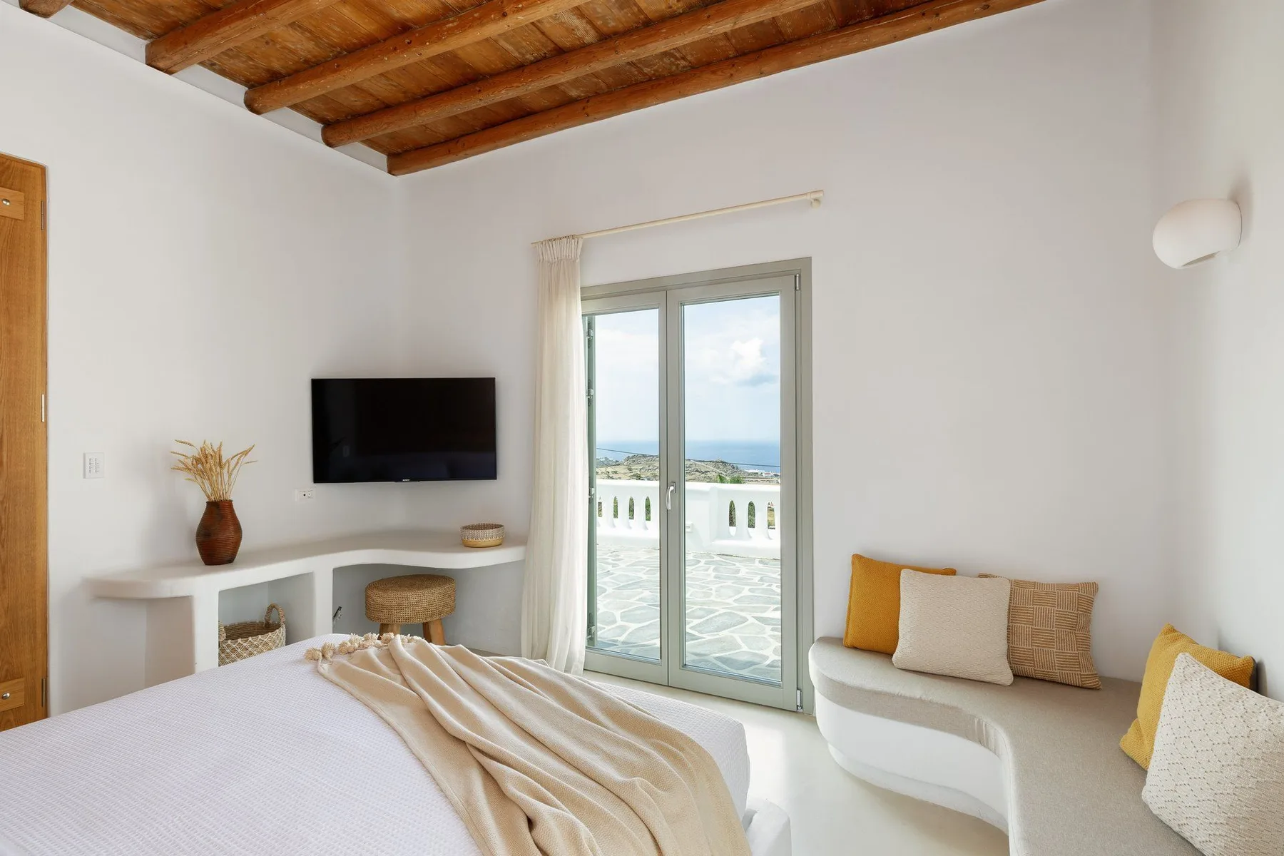 A bedroom with a bed, television, and glass doors opening onto a balcony.