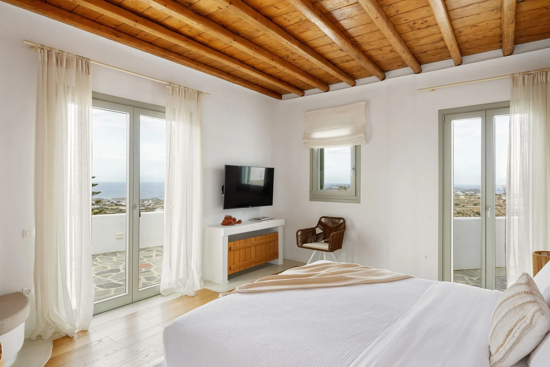 A bright bedroom with a bed, television, and sliding glass doors opening to a balcony.