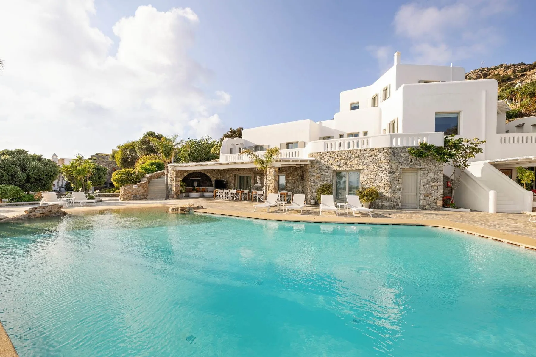 A turquoise swimming pool sits in front of a white resort building.