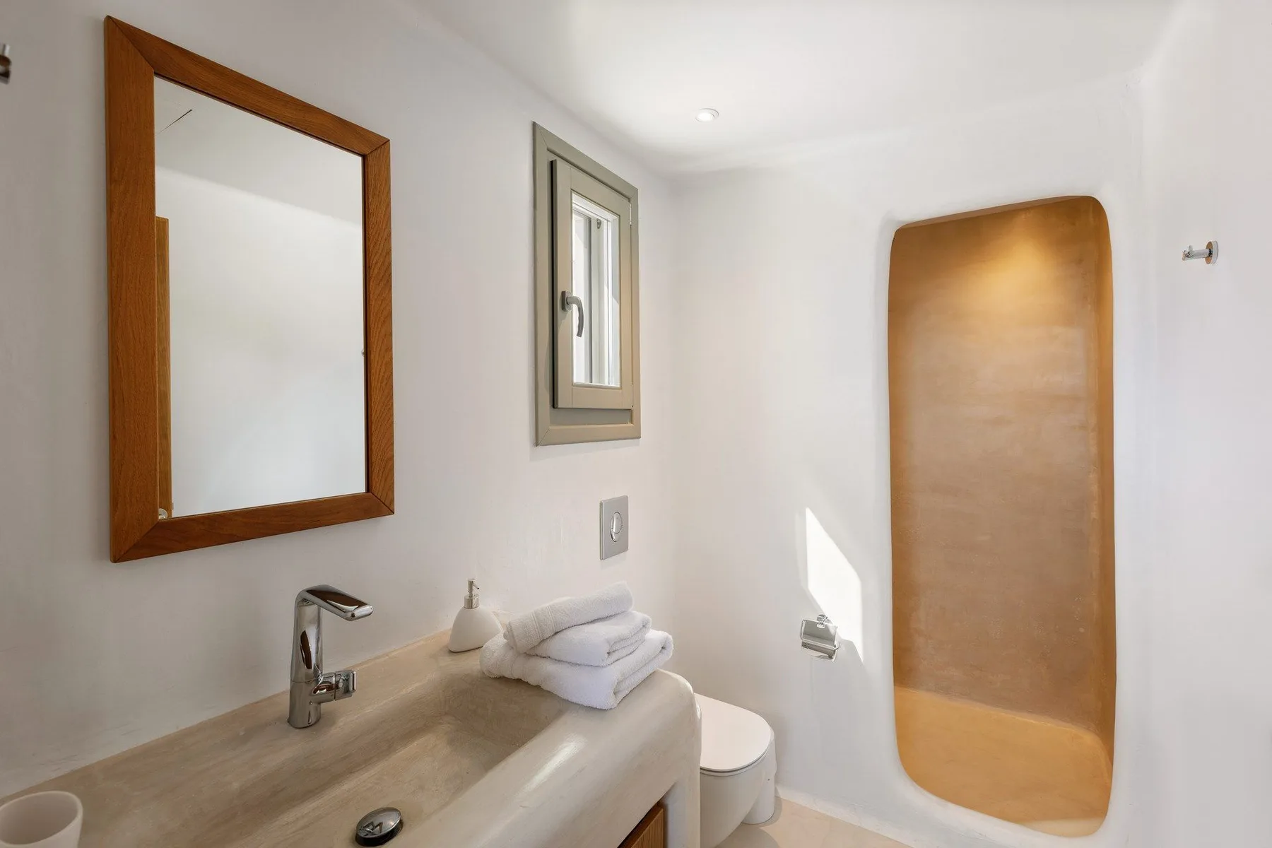 A bright bathroom with a sink, mirror, and recessed shower area.