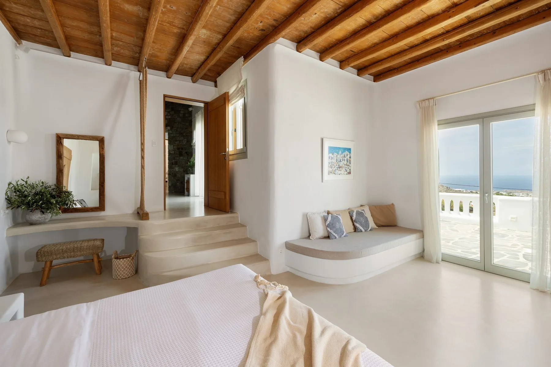 A bright bedroom opens onto a sitting area and balcony with a sea view.