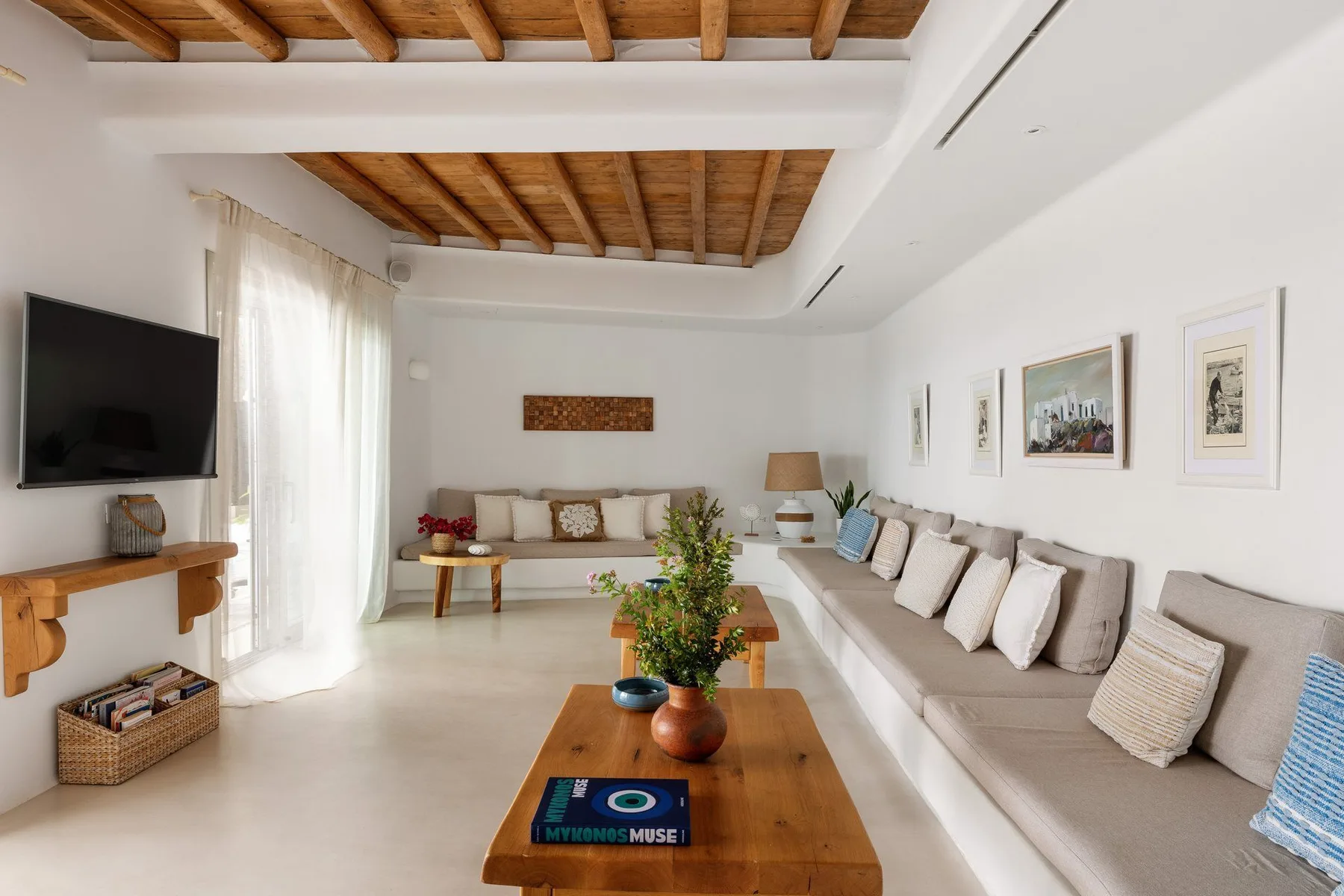 A bright living room with long seating, a wooden coffee table, and exposed ceiling beams.