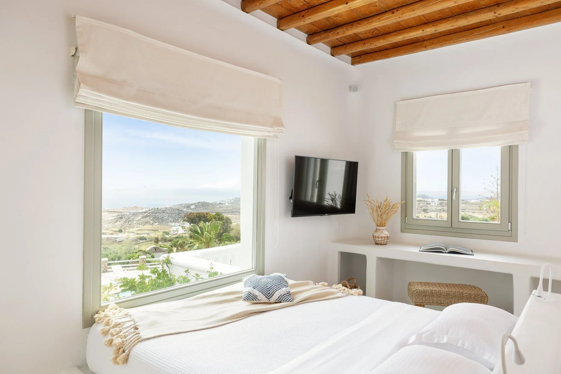 A bright bedroom with a bed, two windows, and a wall-mounted television.