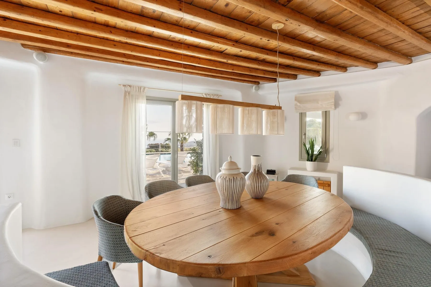 A dining area with a large wooden table beneath exposed ceiling beams.