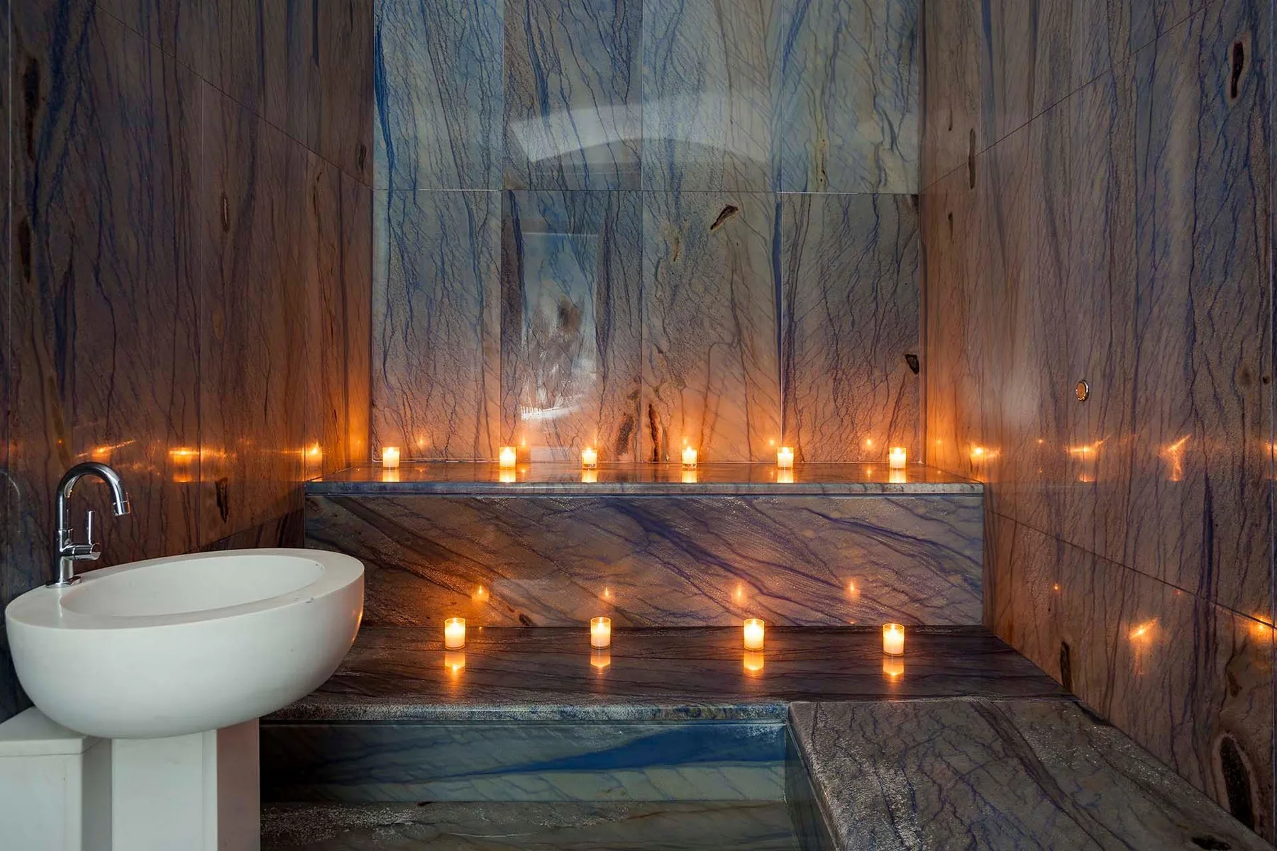 A marble bathroom features a soaking tub, a shower, and rows of candles.