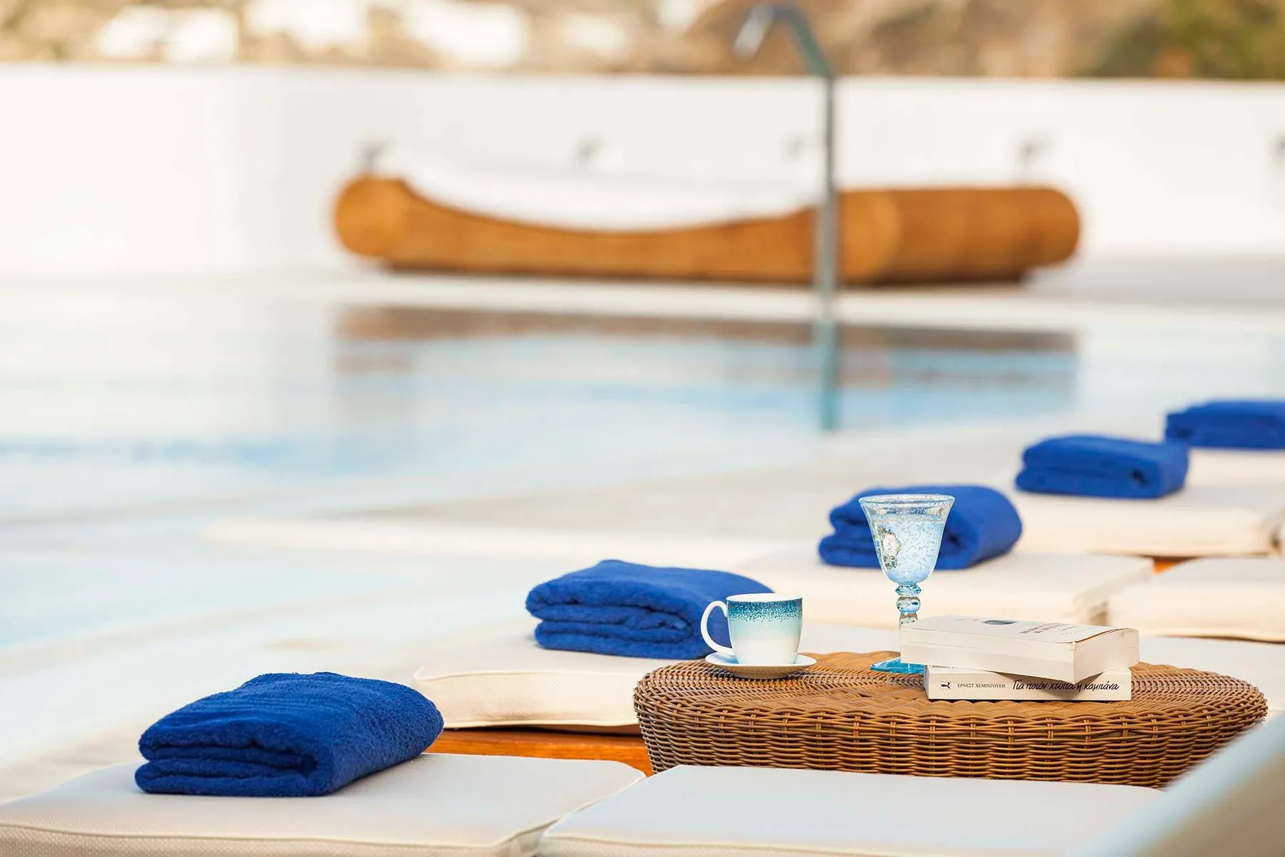 Poolside seating with folded blue towels and a small table set with cups.