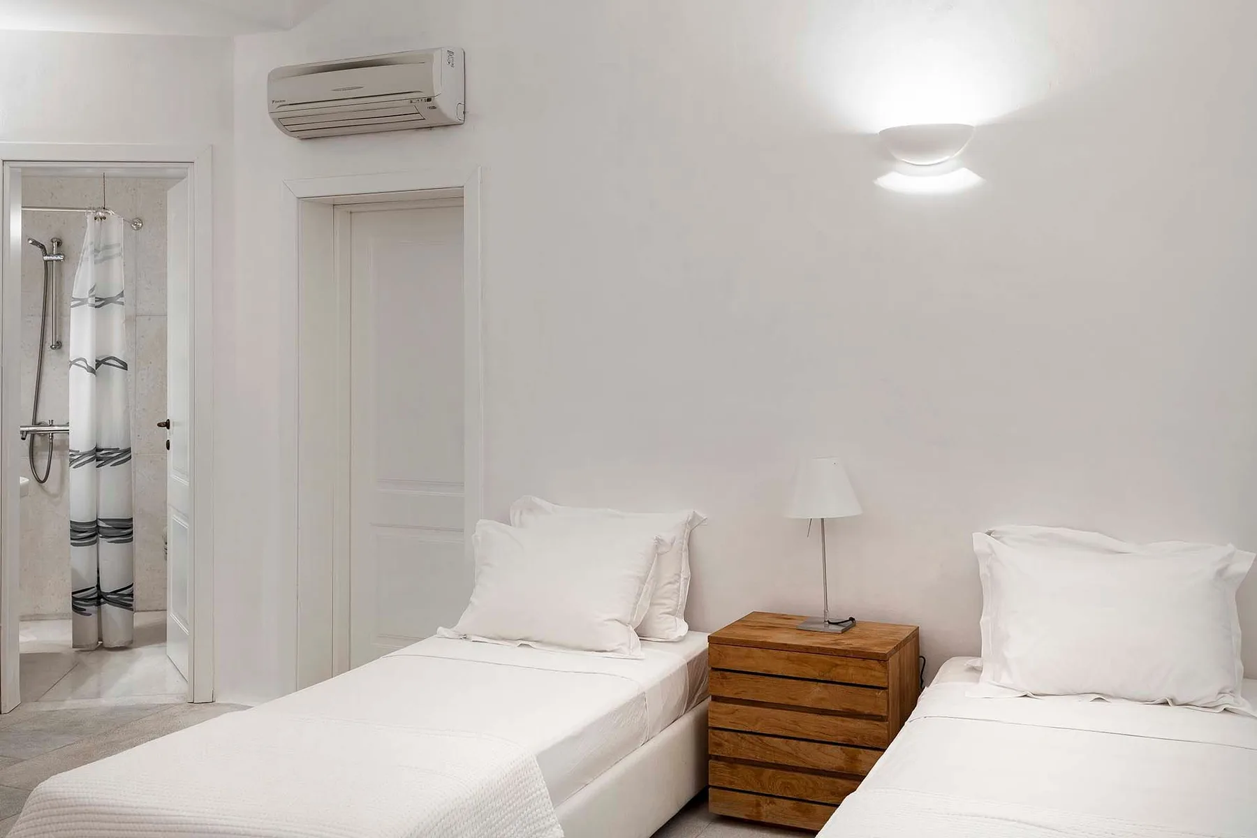 A bright bedroom with two beds and a wooden bedside table.