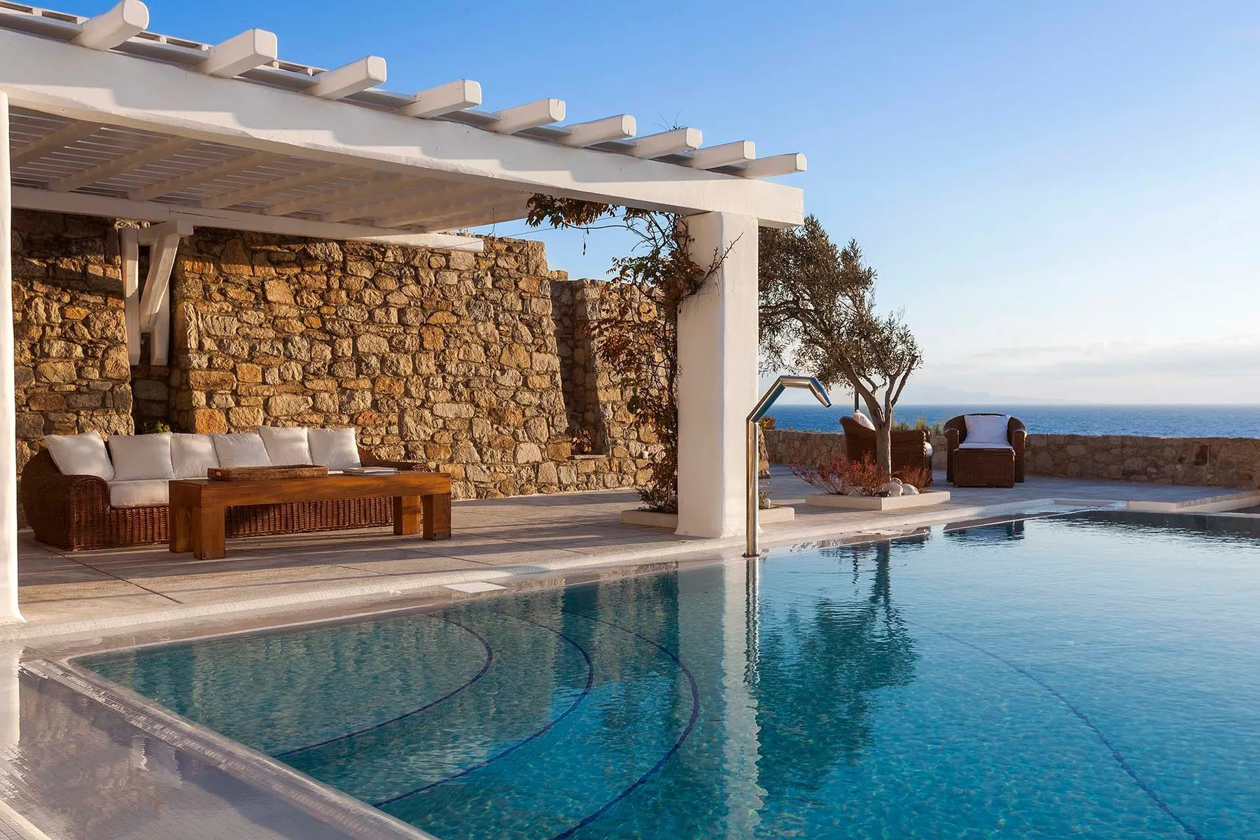 A swimming pool beside a covered outdoor seating area and stone wall.