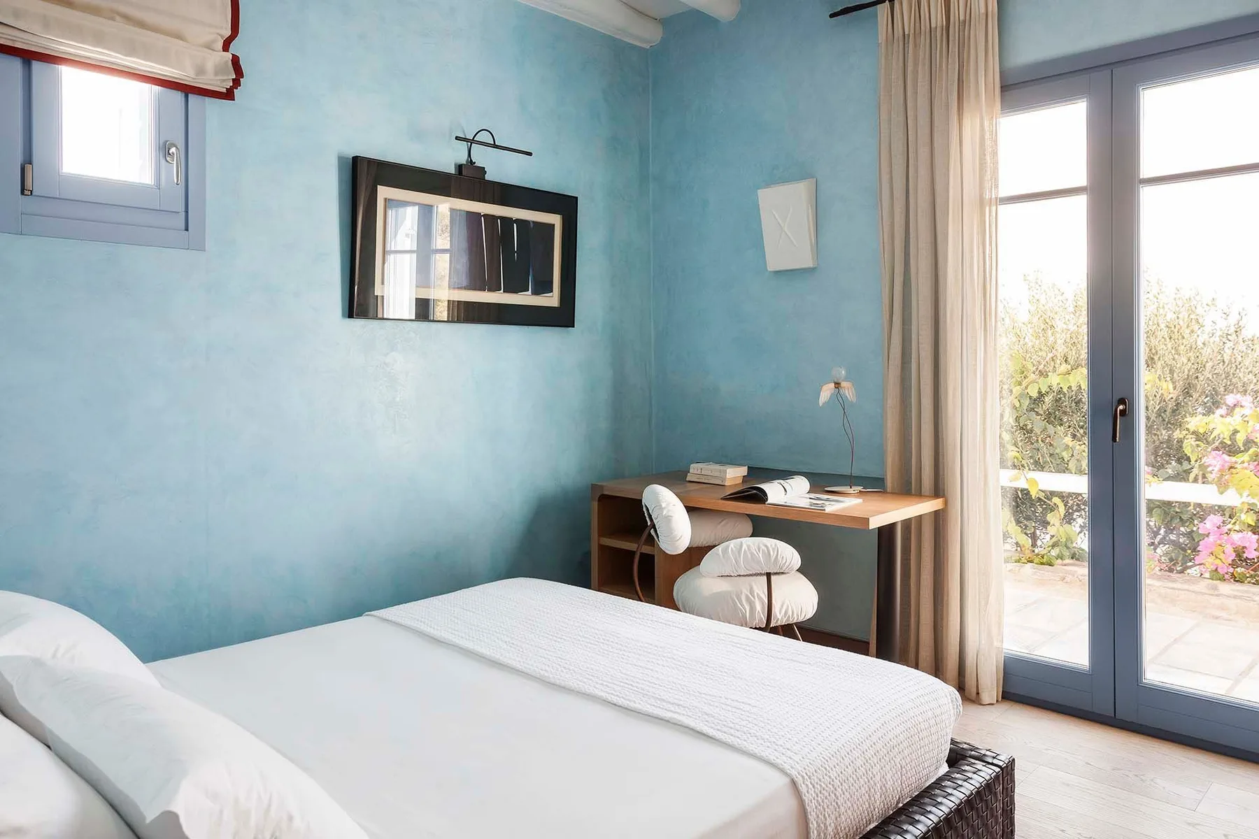 A bedroom with a bed, a small desk, and glass doors opening onto a patio.
