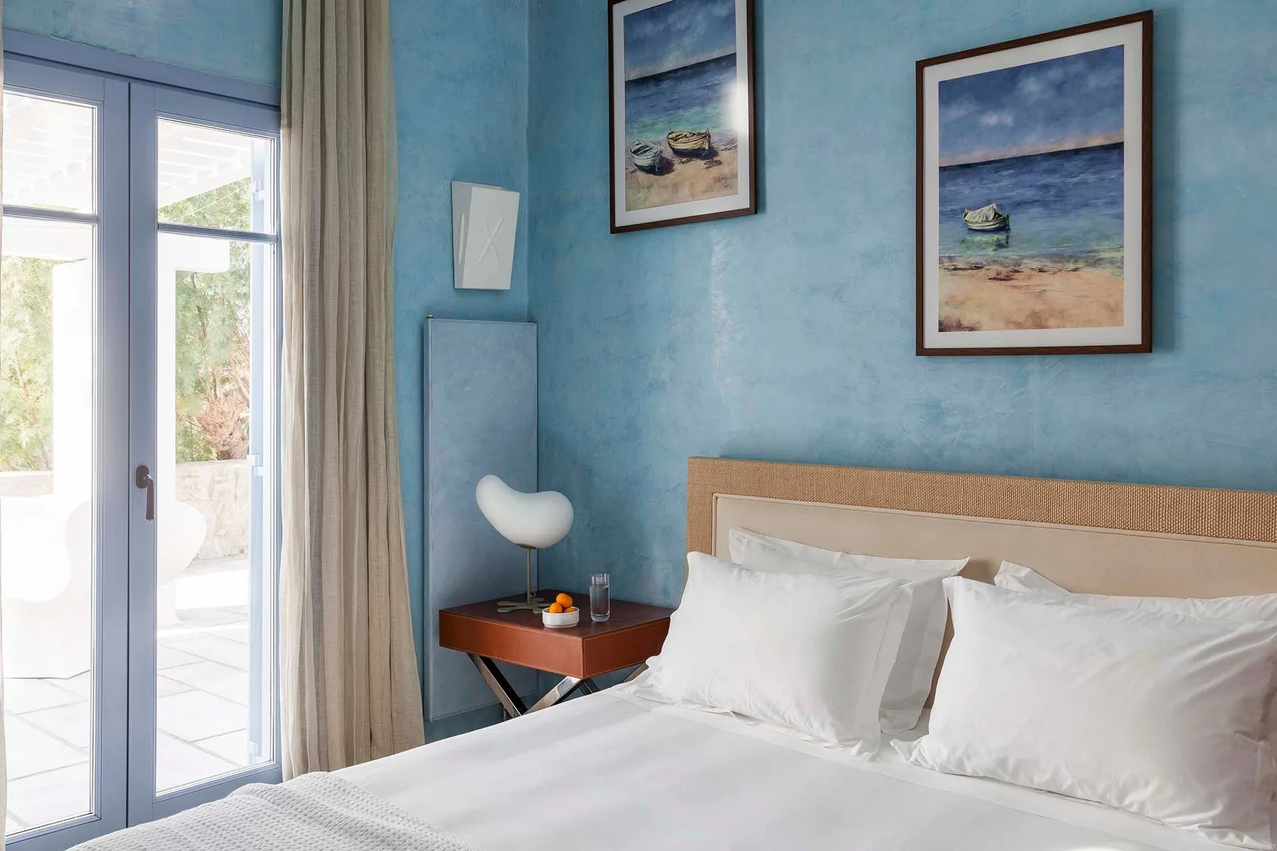 A bedroom with a bed, blue walls, and framed artwork.