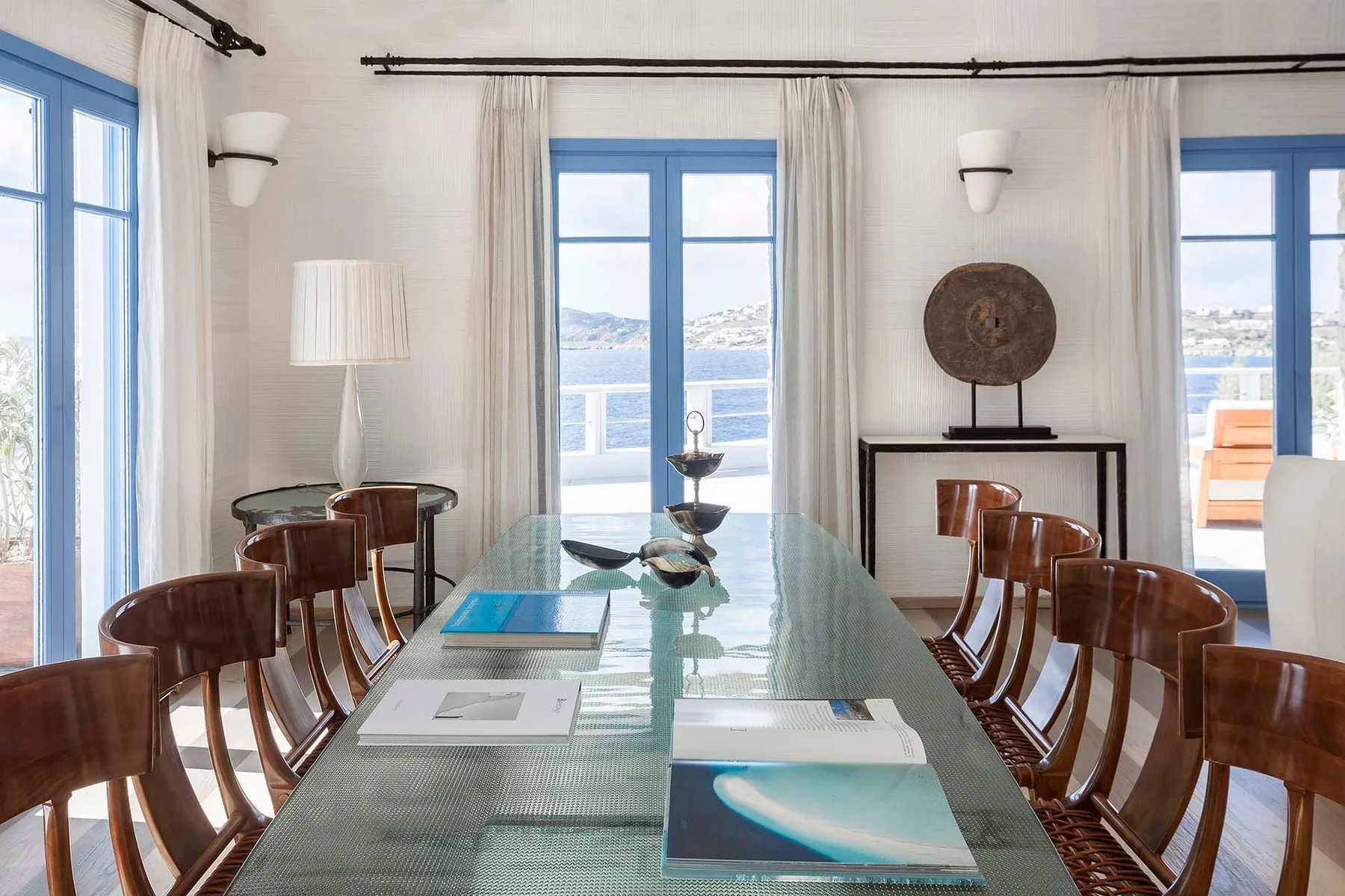 A dining room with a long table and wooden seating beside large windows.
