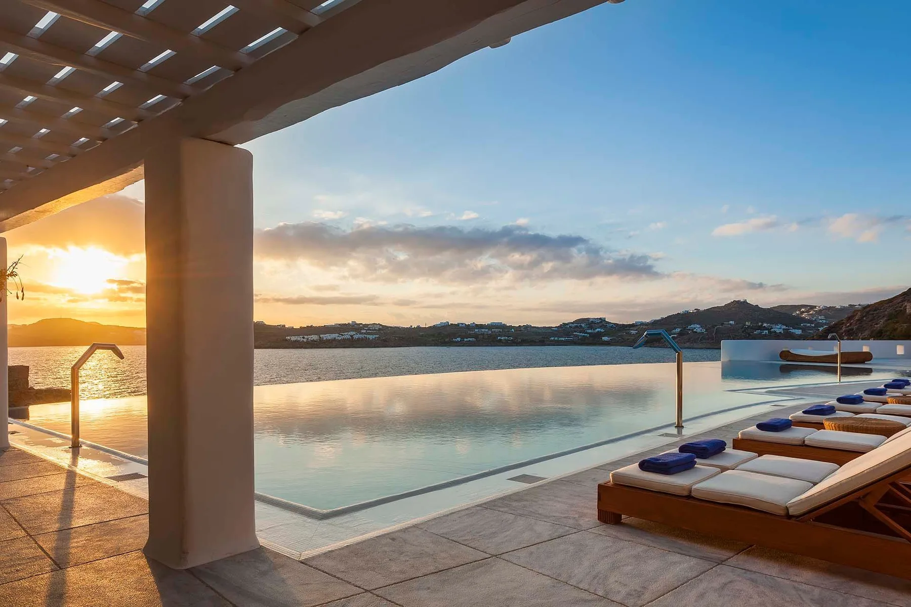 An outdoor pool overlooks a lake at sunset, with lounge seating along the edge.