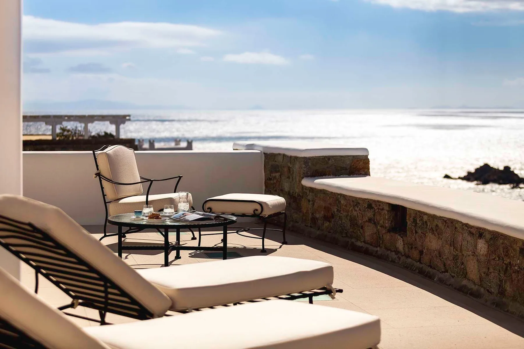 A seaside terrace with lounge seating and a low table overlooks the ocean.
