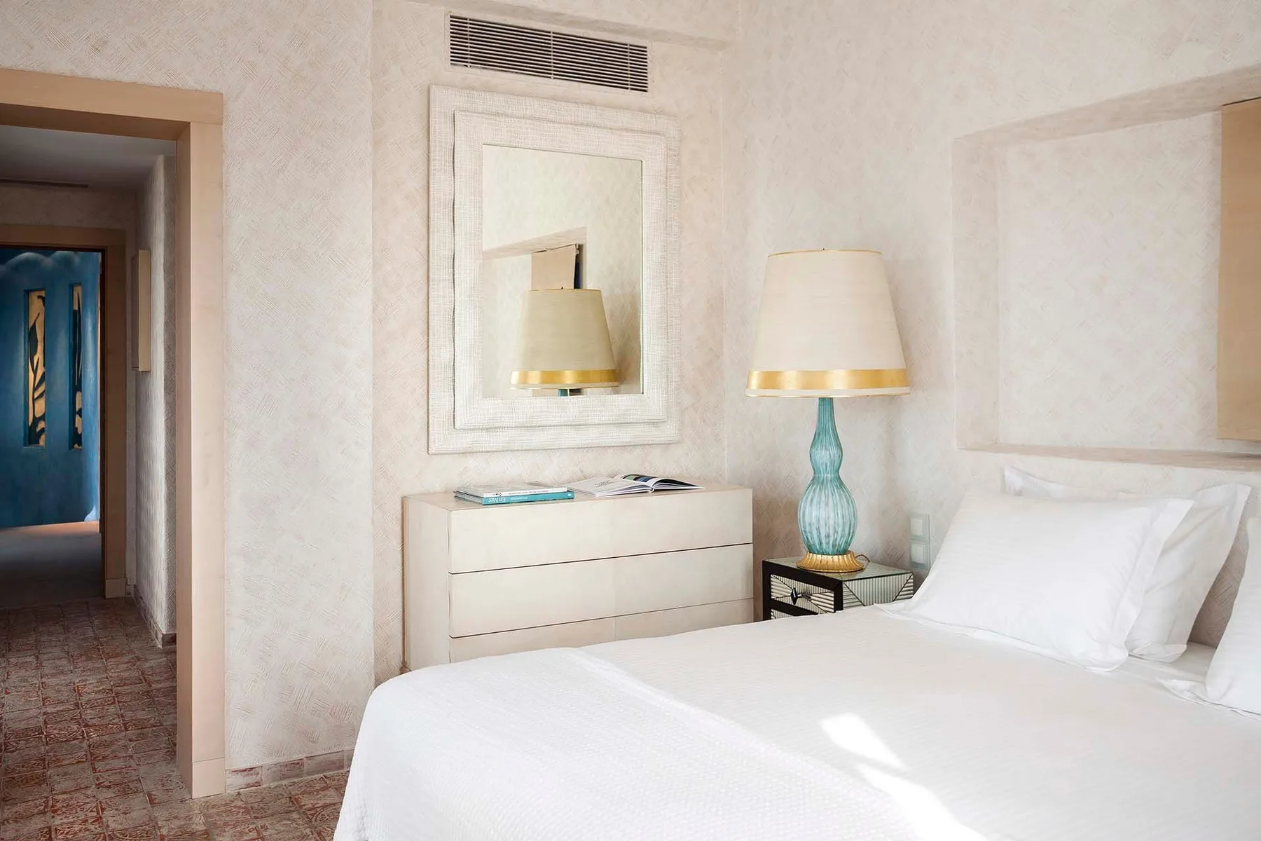 A bright bedroom with white bedding and a bedside lamp.