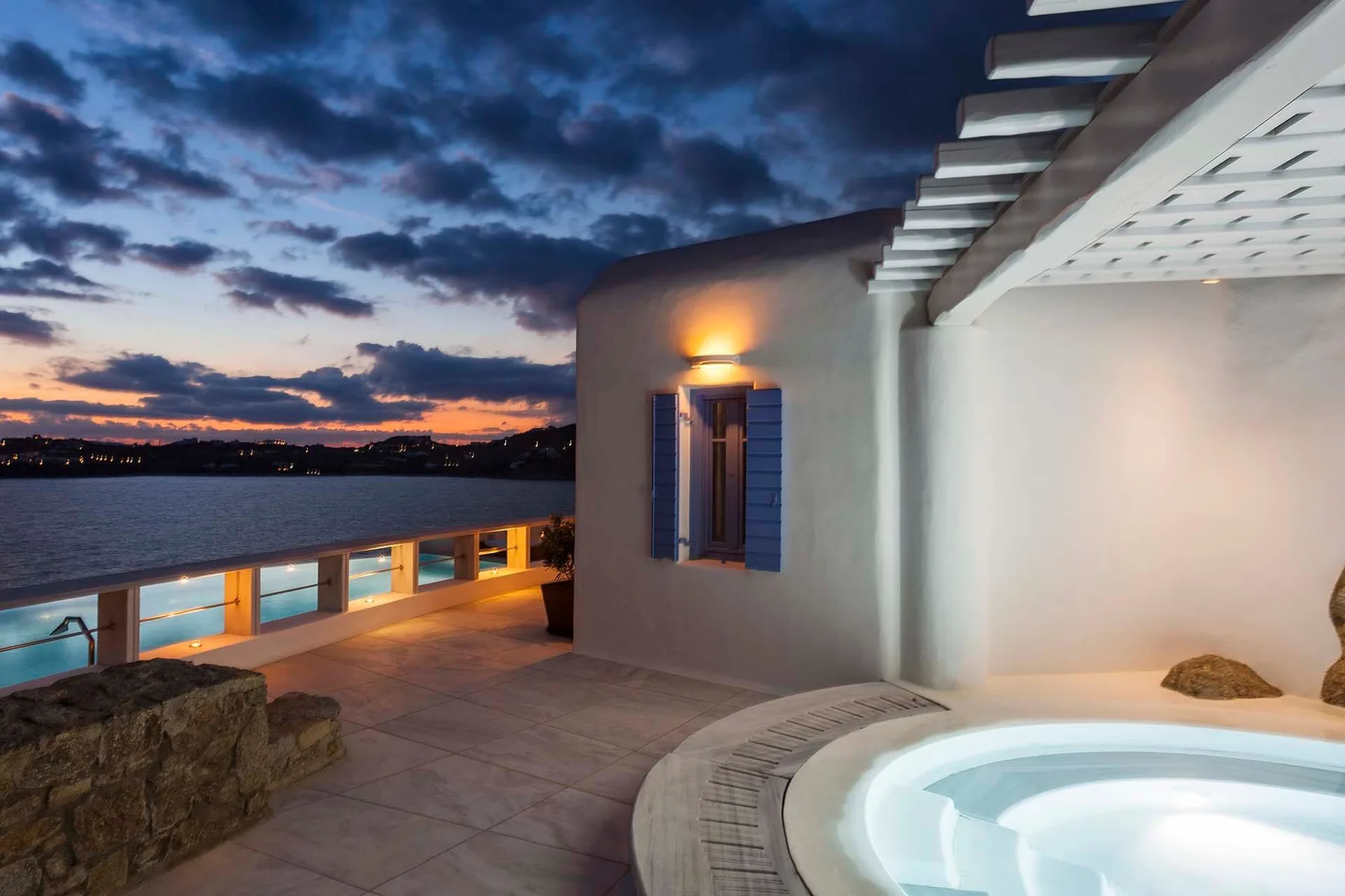 A terrace beside a round hot tub overlooks the water at sunset.
