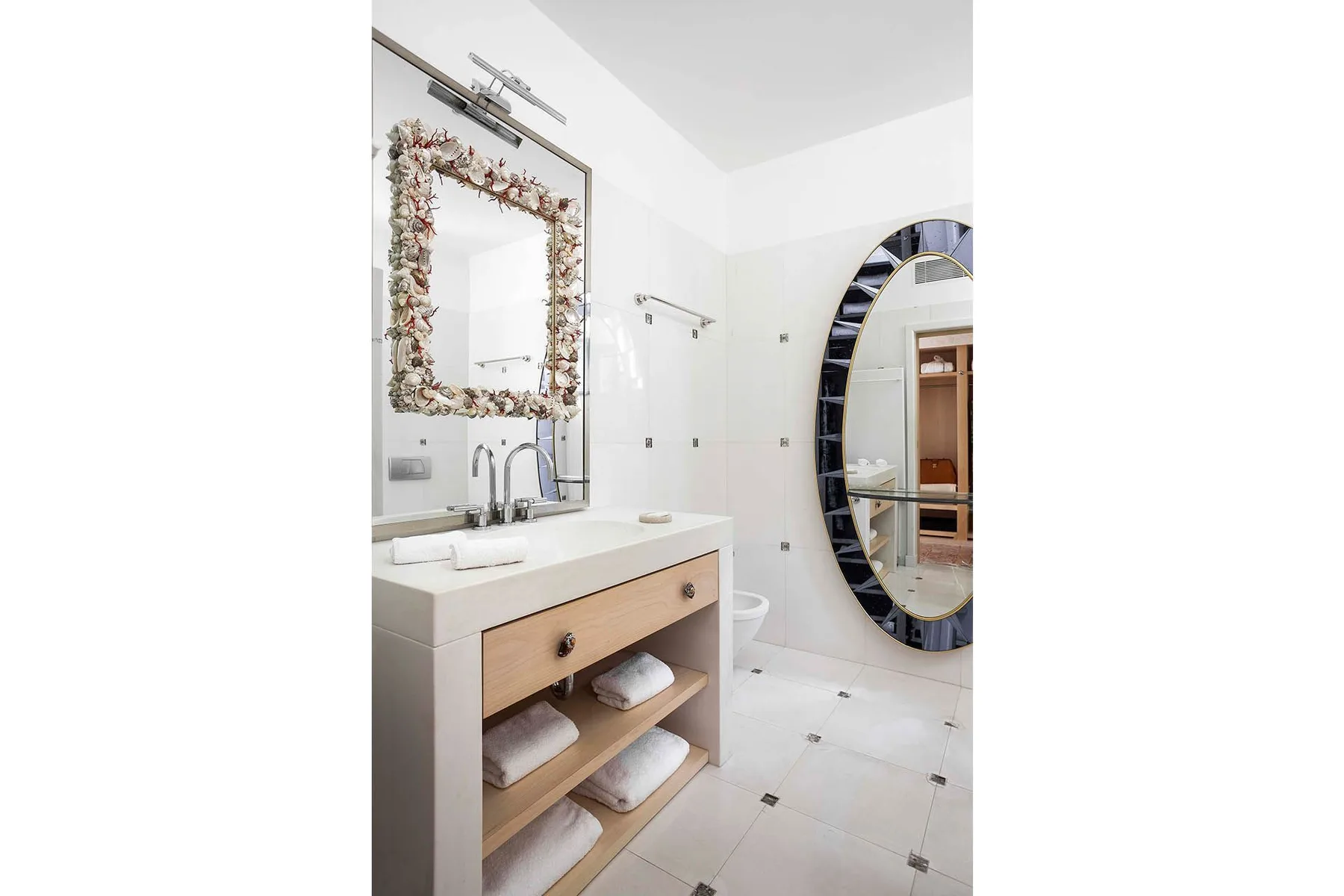 A bright bathroom with a sink vanity and a large oval mirror.