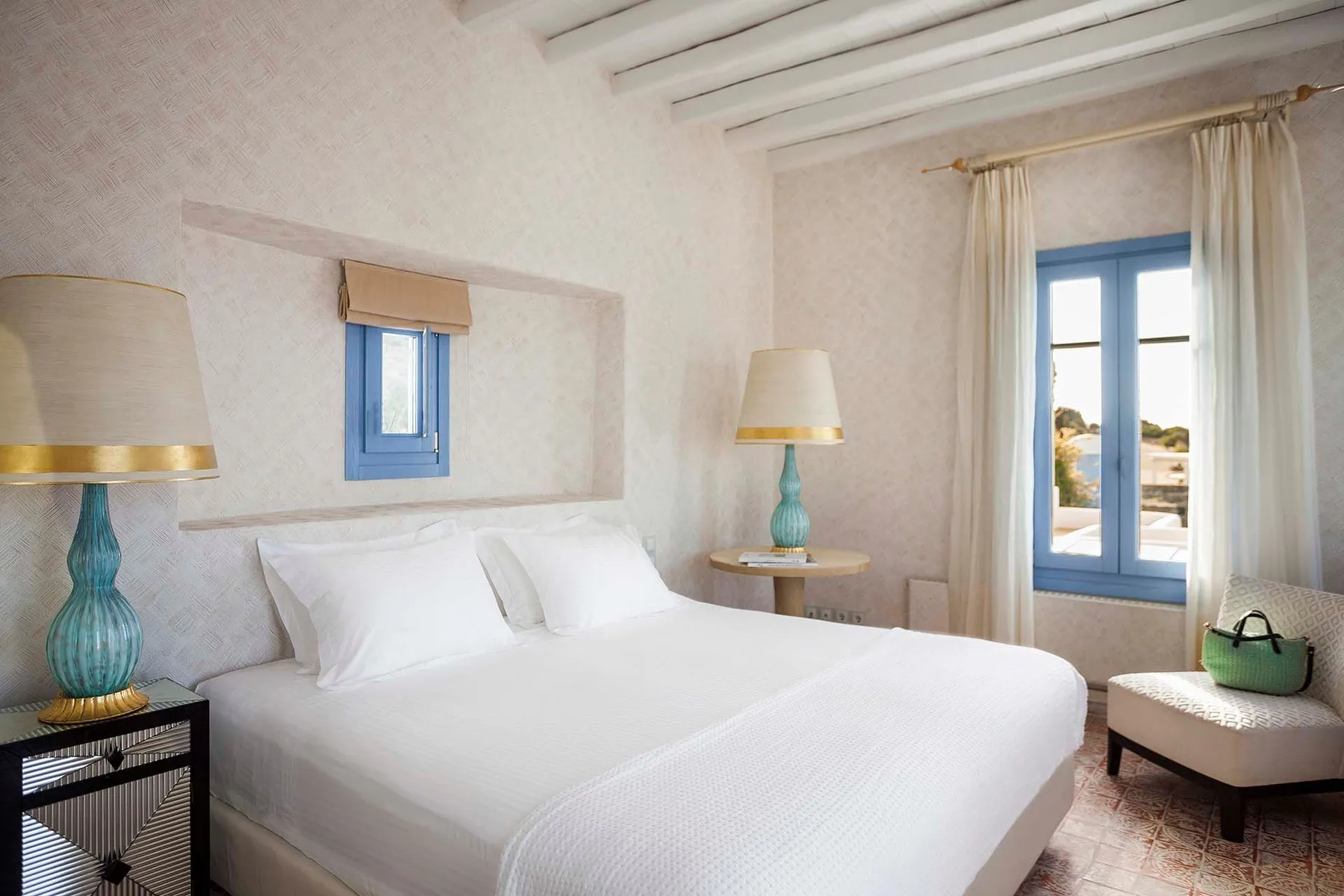 A bright bedroom with a white bed and blue-framed windows.