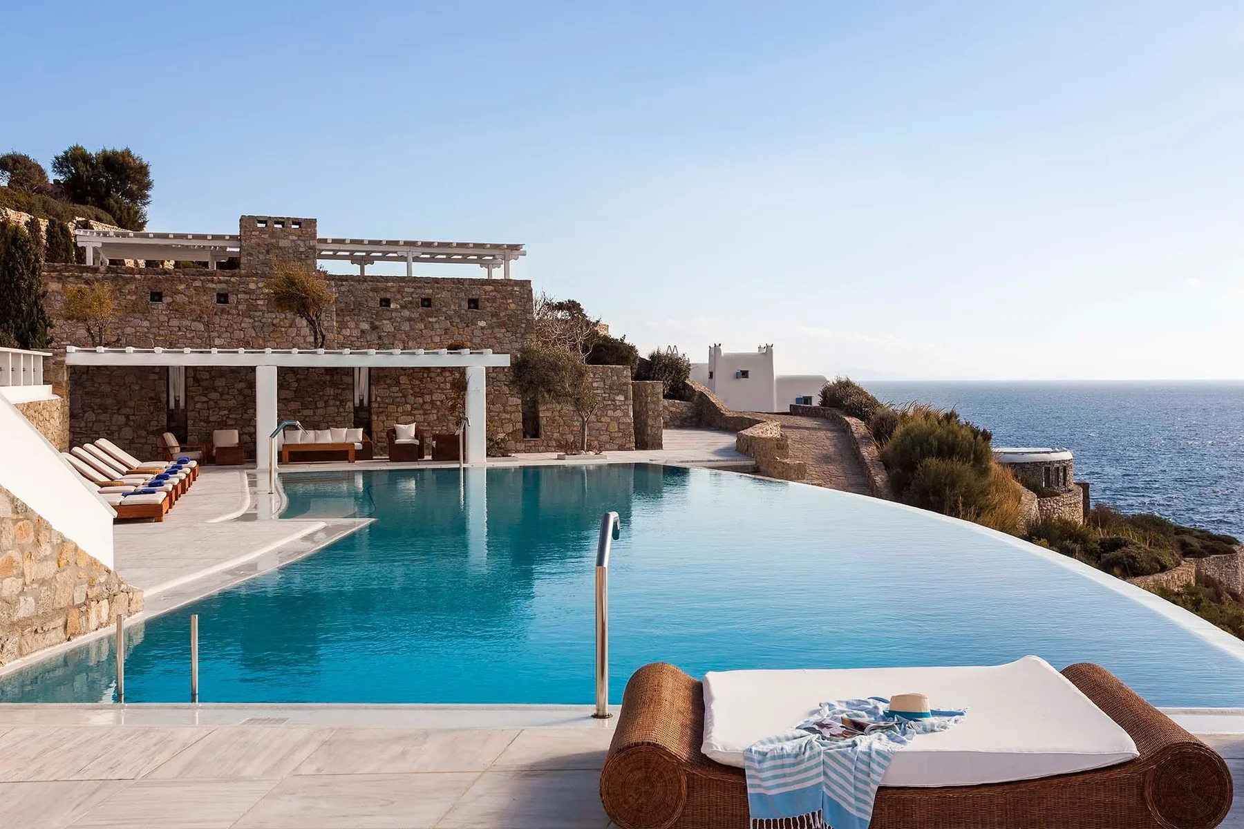 An outdoor infinity pool beside a stone building overlooks the sea.