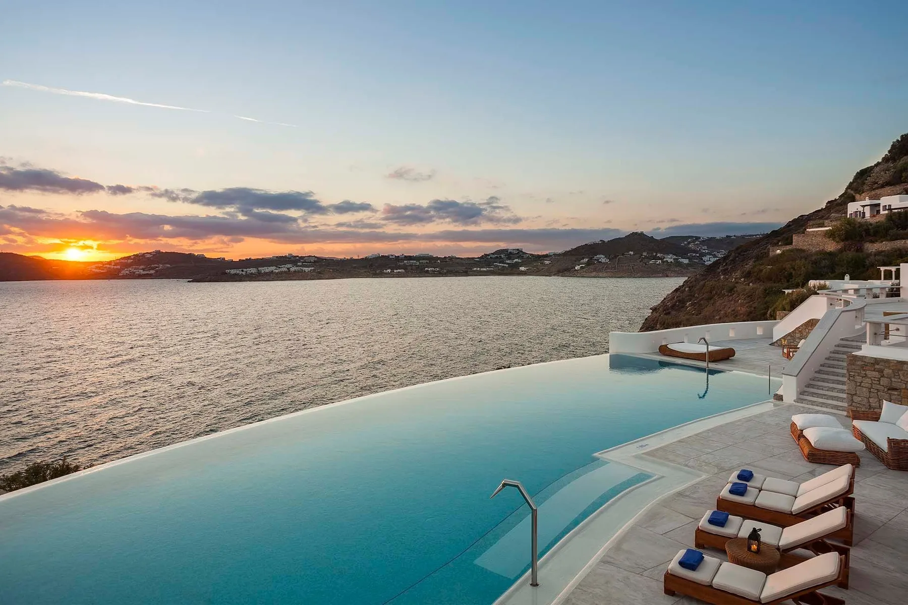 An infinity pool overlooks the sea at sunset, with loungers beside the water.