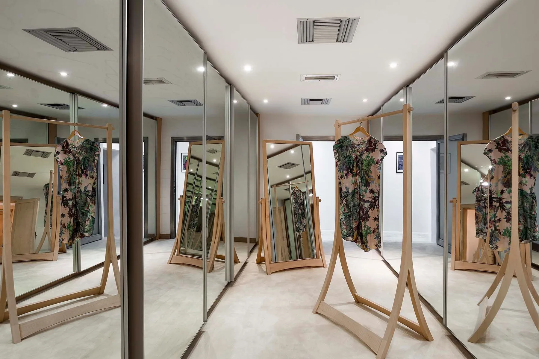 A mirrored dressing room with clothing displayed on freestanding racks.