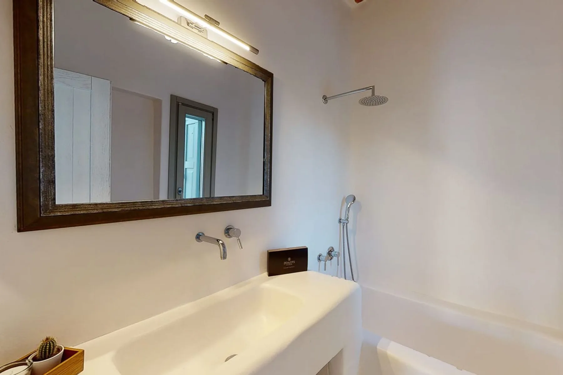 A bathroom with a bathtub, wall-mounted shower, and large mirror.