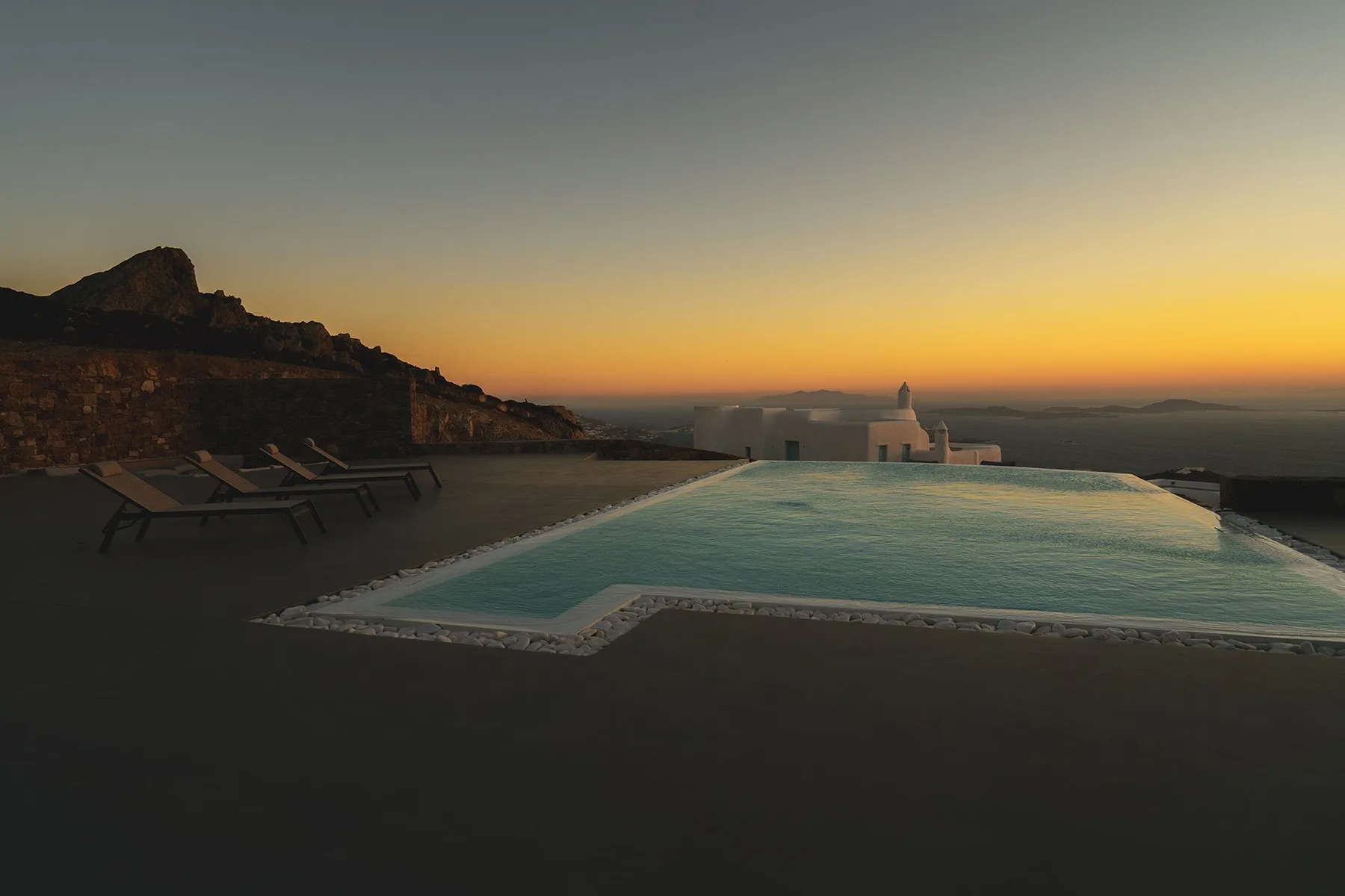 An outdoor pool overlooks a coastal landscape at sunset.