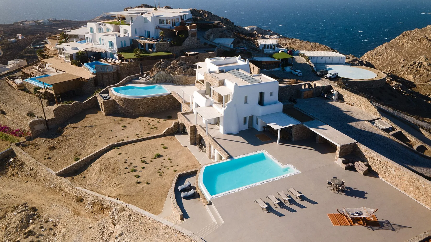 Aerial view of white buildings and swimming pools along a rocky coastline.