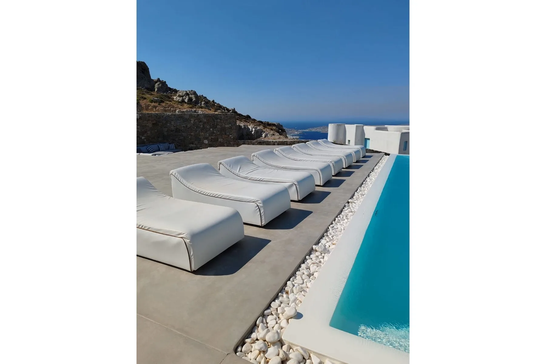A poolside terrace with white loungers beside a blue swimming pool.