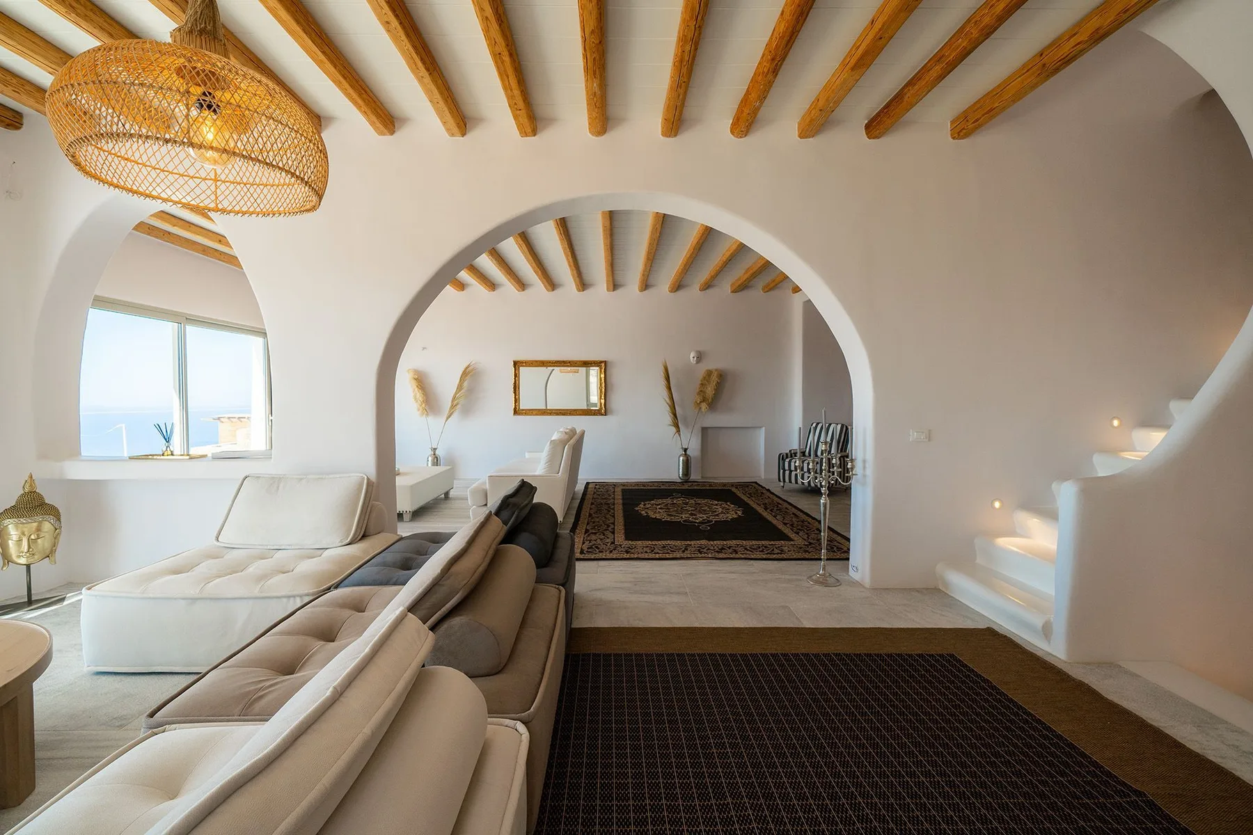 A bright living room with arched openings, seating, and exposed ceiling beams.
