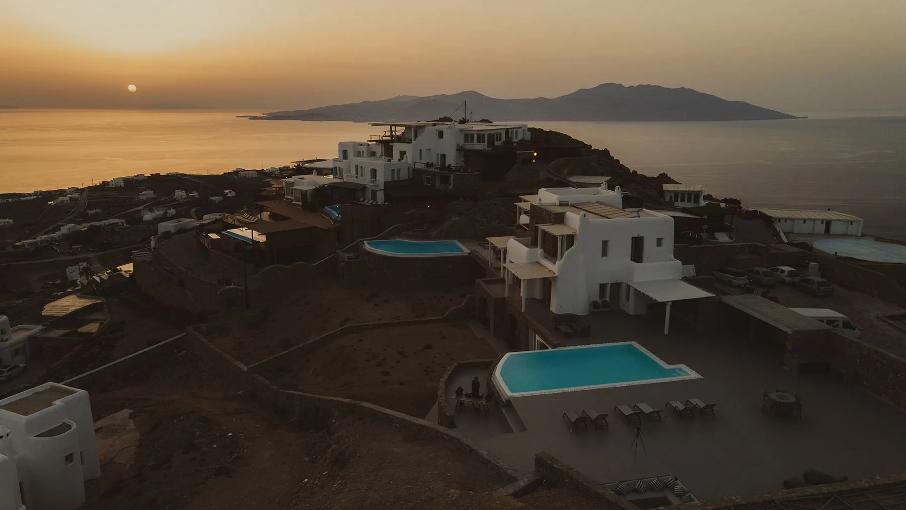 White buildings and turquoise pools sit on a coastal hillside at sunset.