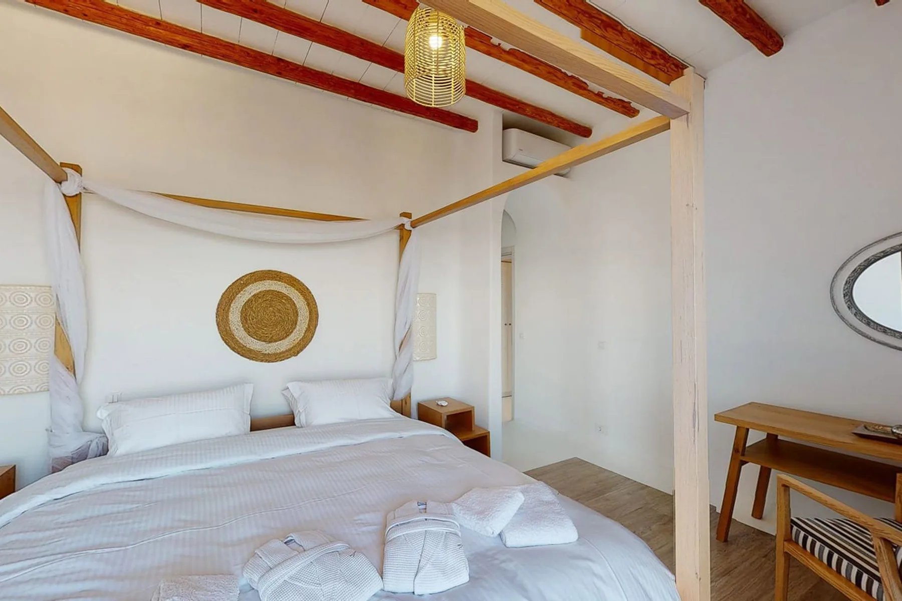 A bedroom with a white bed beneath a fabric canopy and exposed ceiling beams.