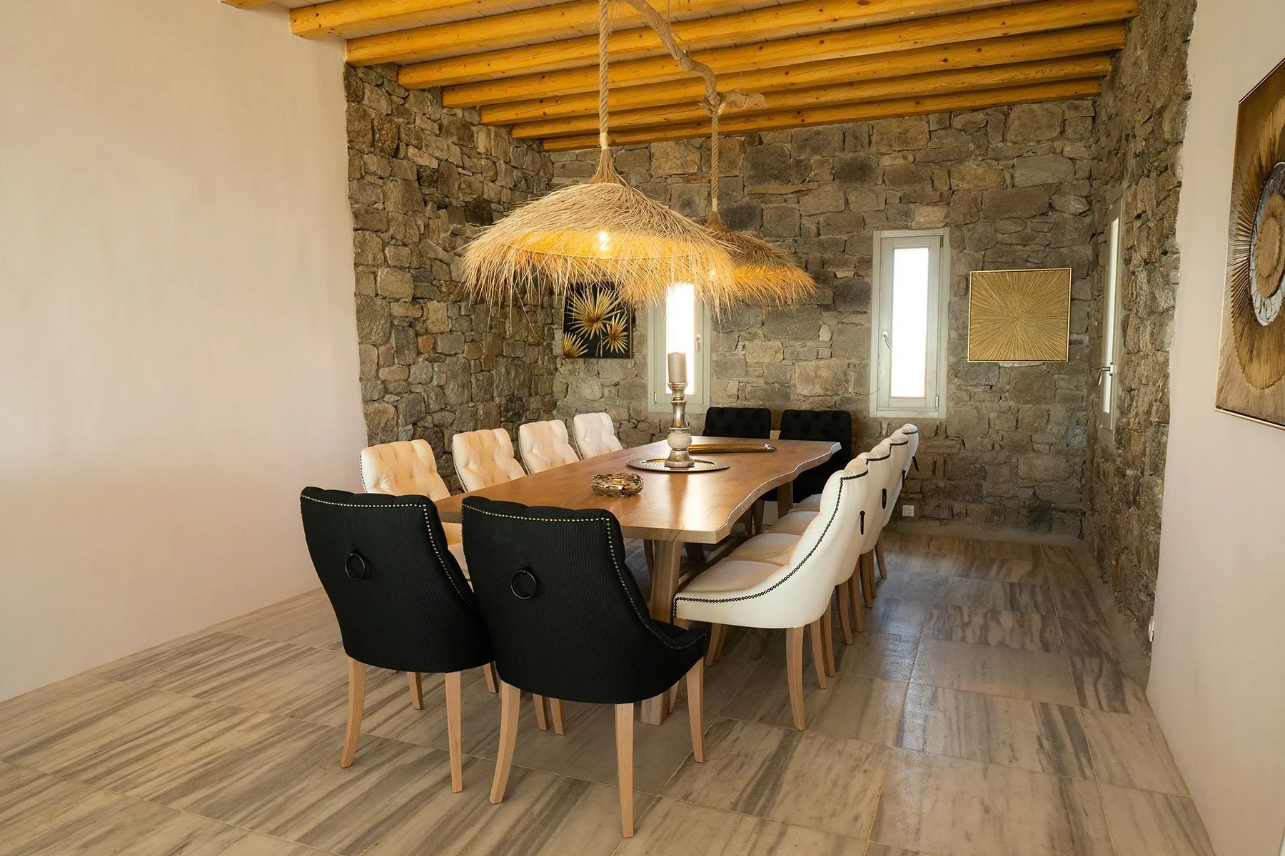 A dining room with a long table and chairs beneath a woven pendant light.