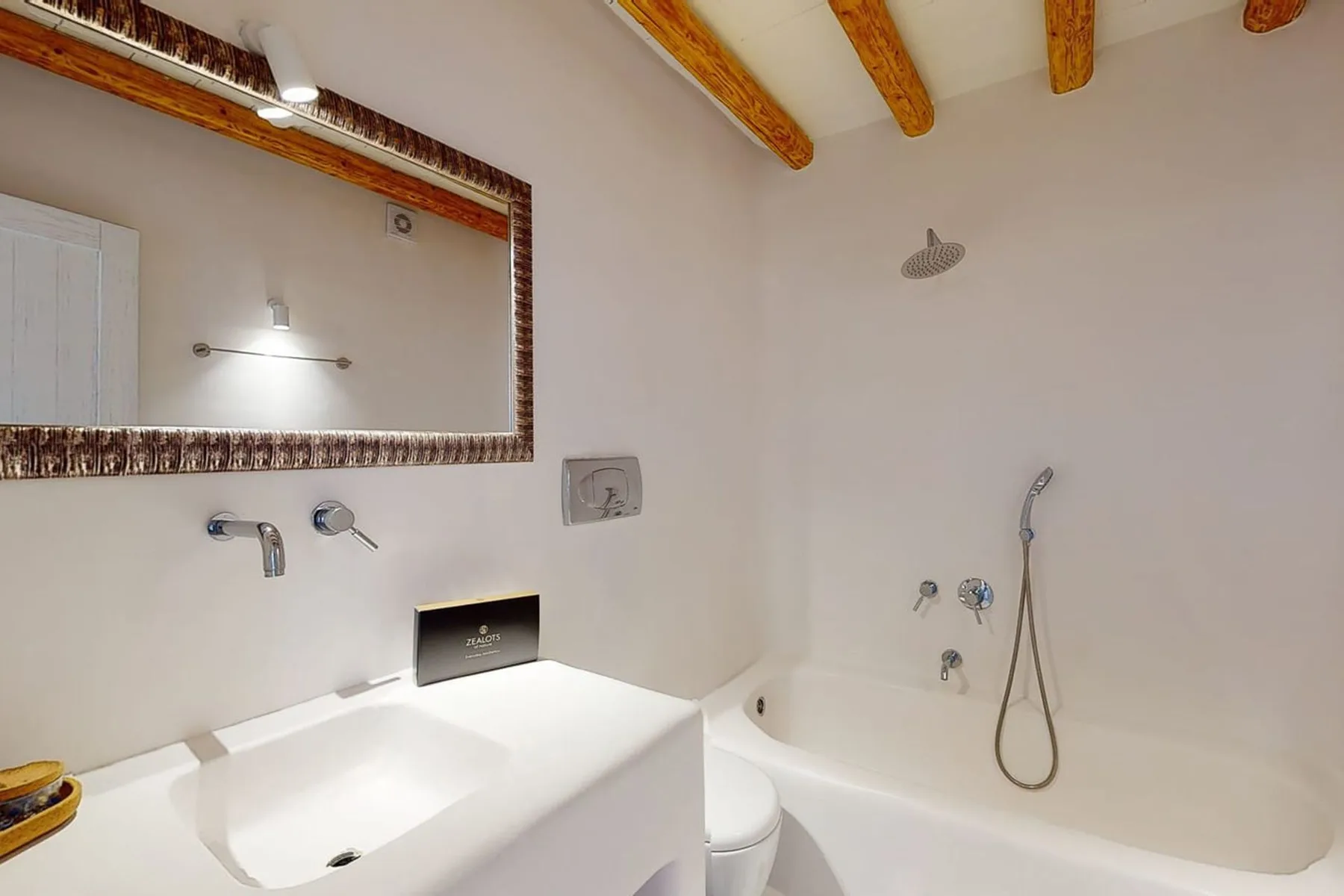 A bathroom with a white sink and bathtub beneath exposed ceiling beams.
