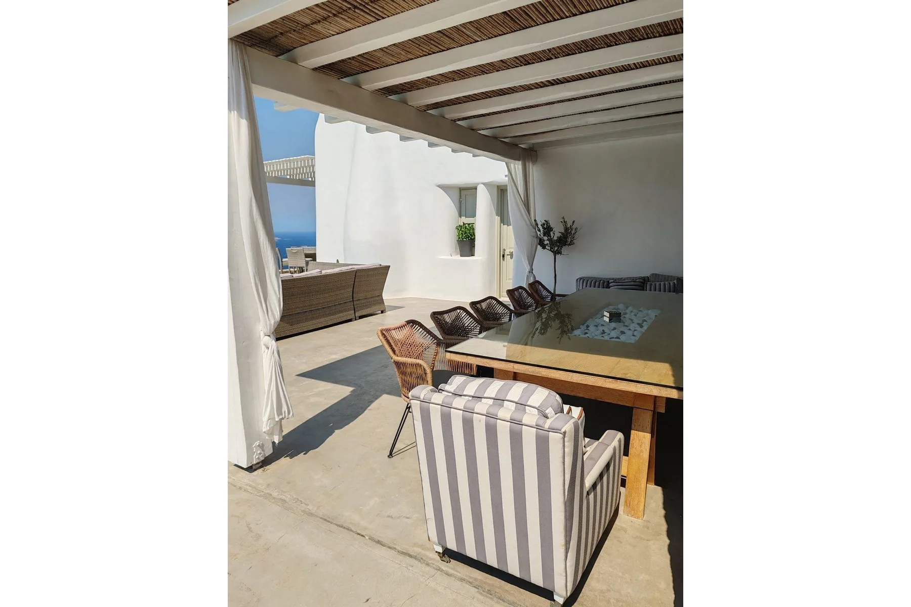 A shaded outdoor dining area with a table and striped seating overlooks the sea.