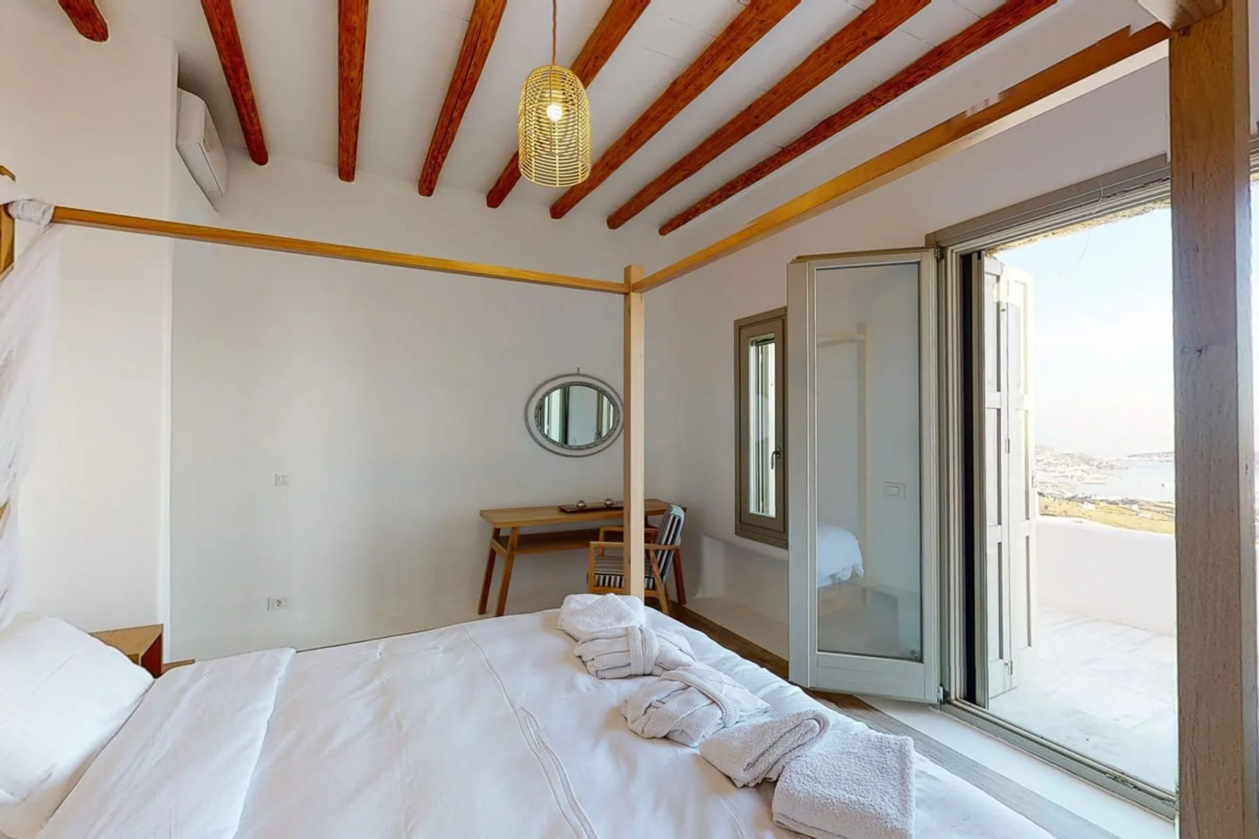 A bright bedroom with a bed, a small desk, and an open glass door.