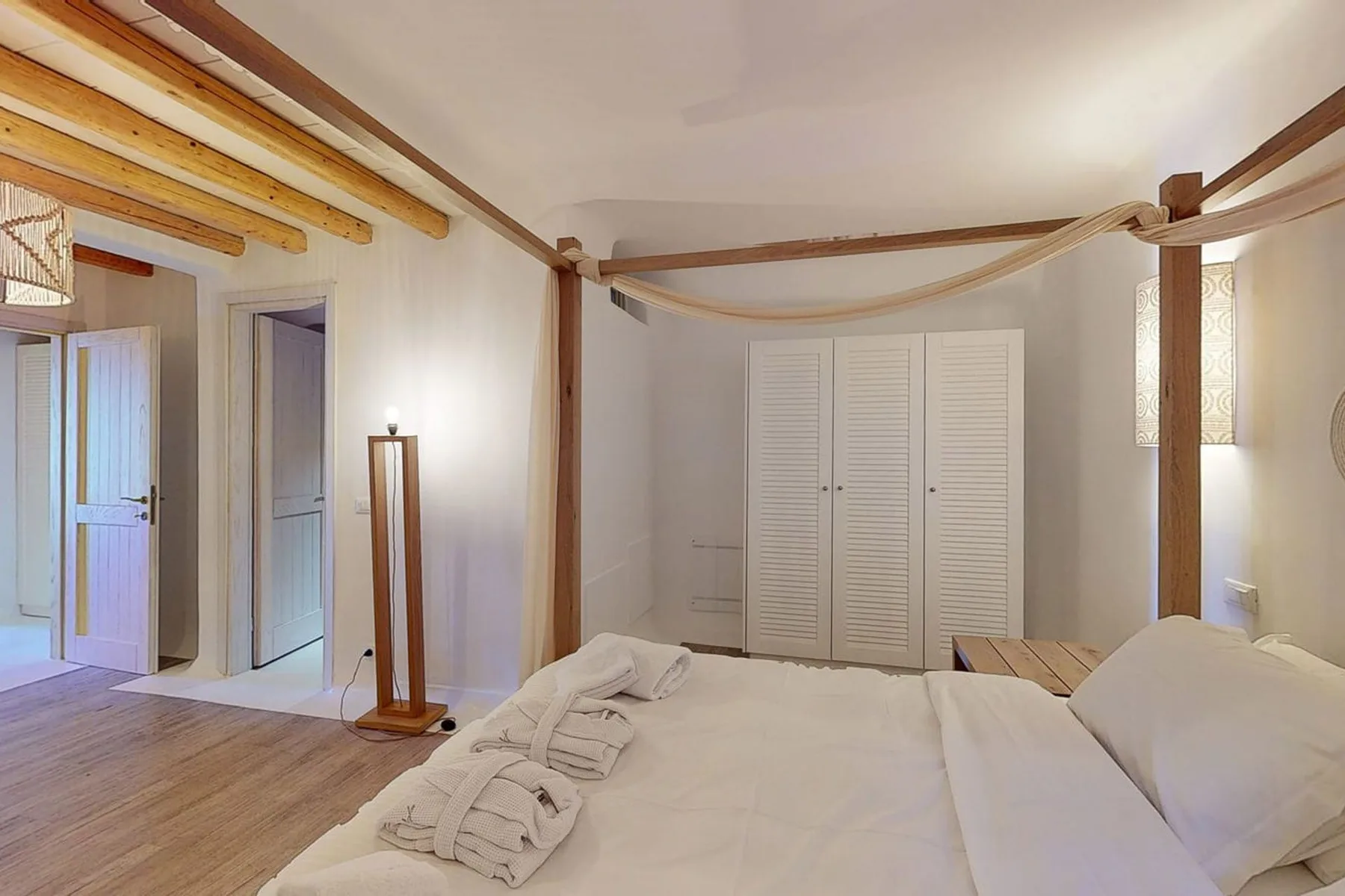 A bedroom with a large bed, white linens, and wooden ceiling beams.