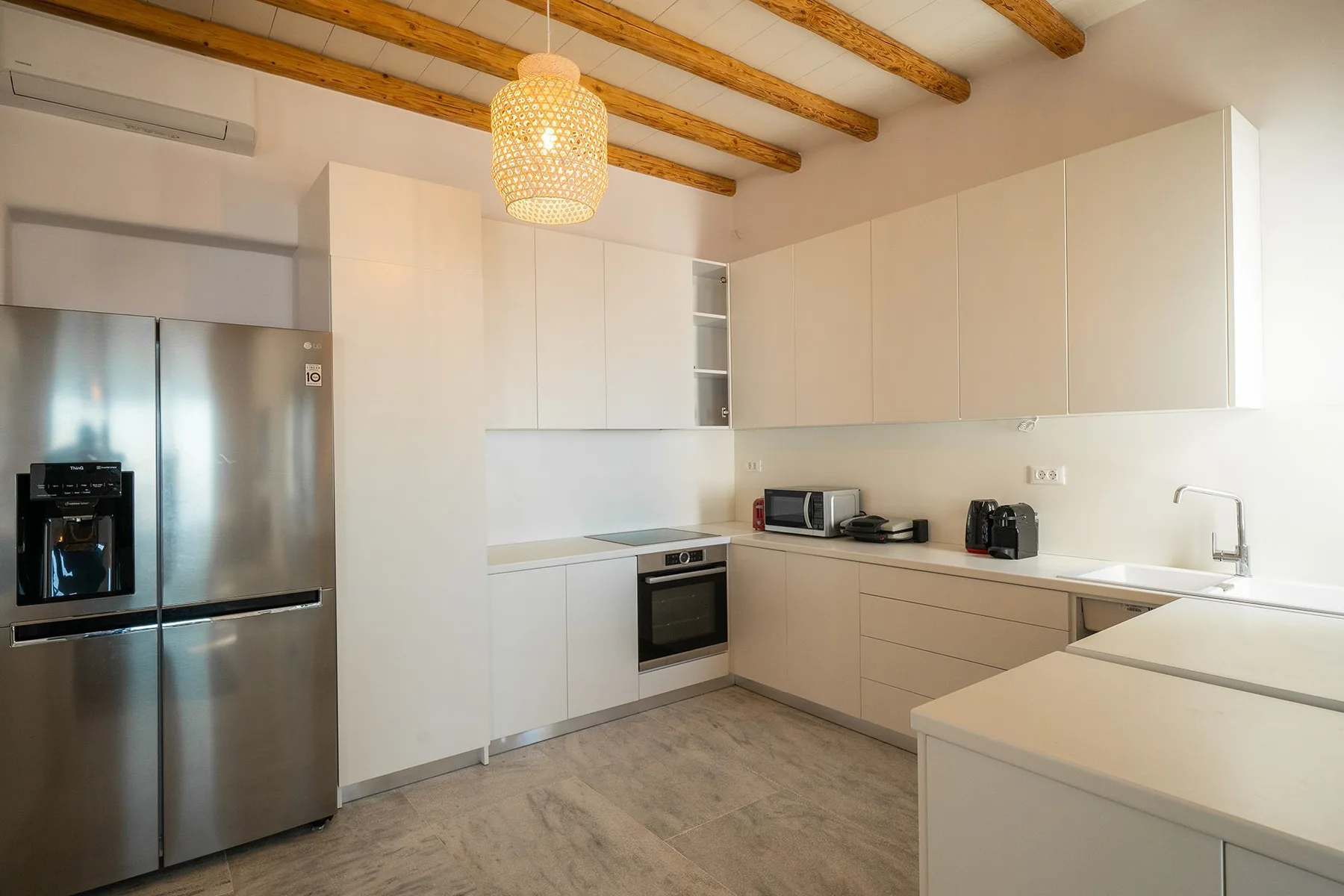 A bright modern kitchen with pale cabinetry, stainless steel appliances, and exposed ceiling beams.