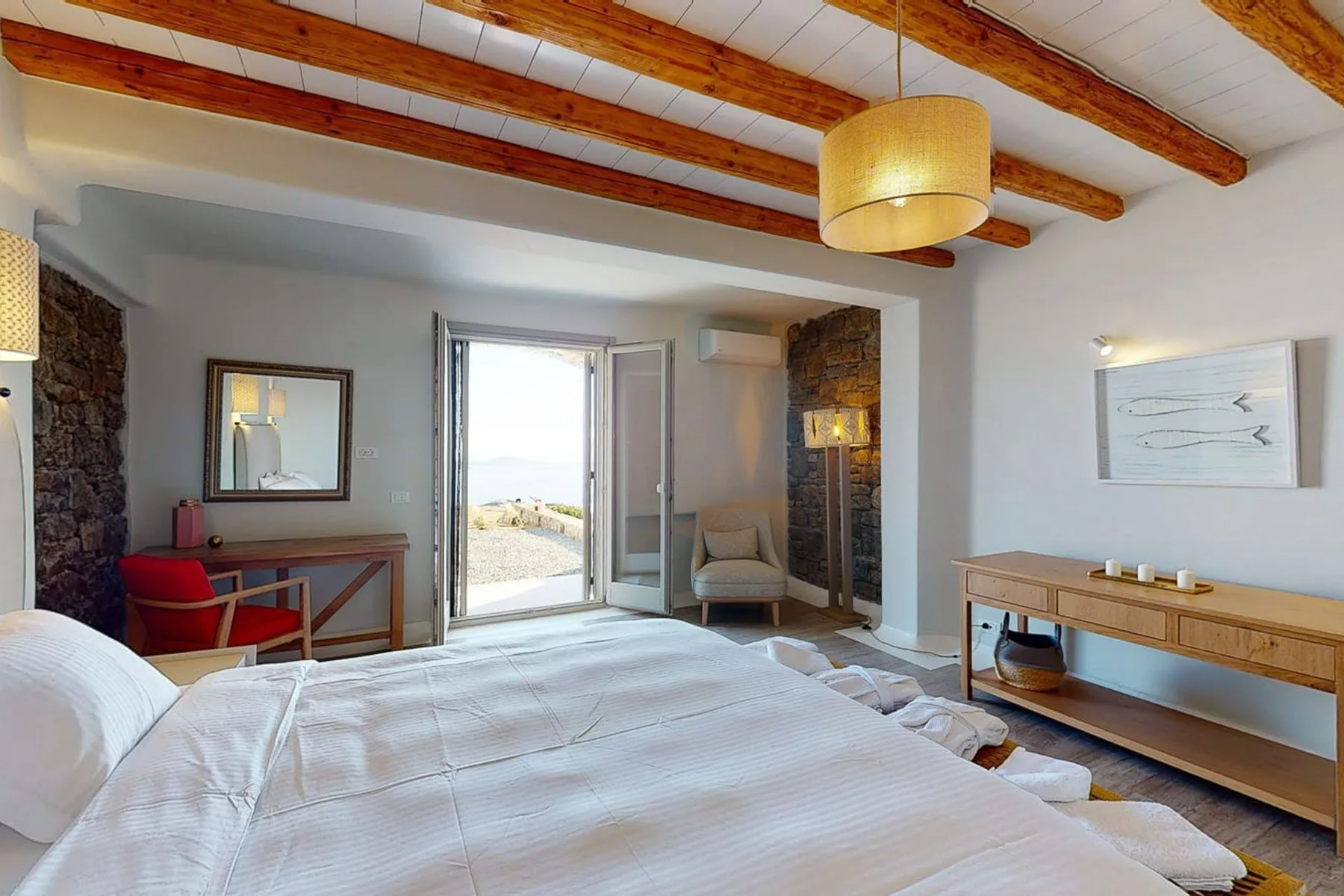 A bedroom with a large bed, wooden ceiling beams, and an open balcony door.