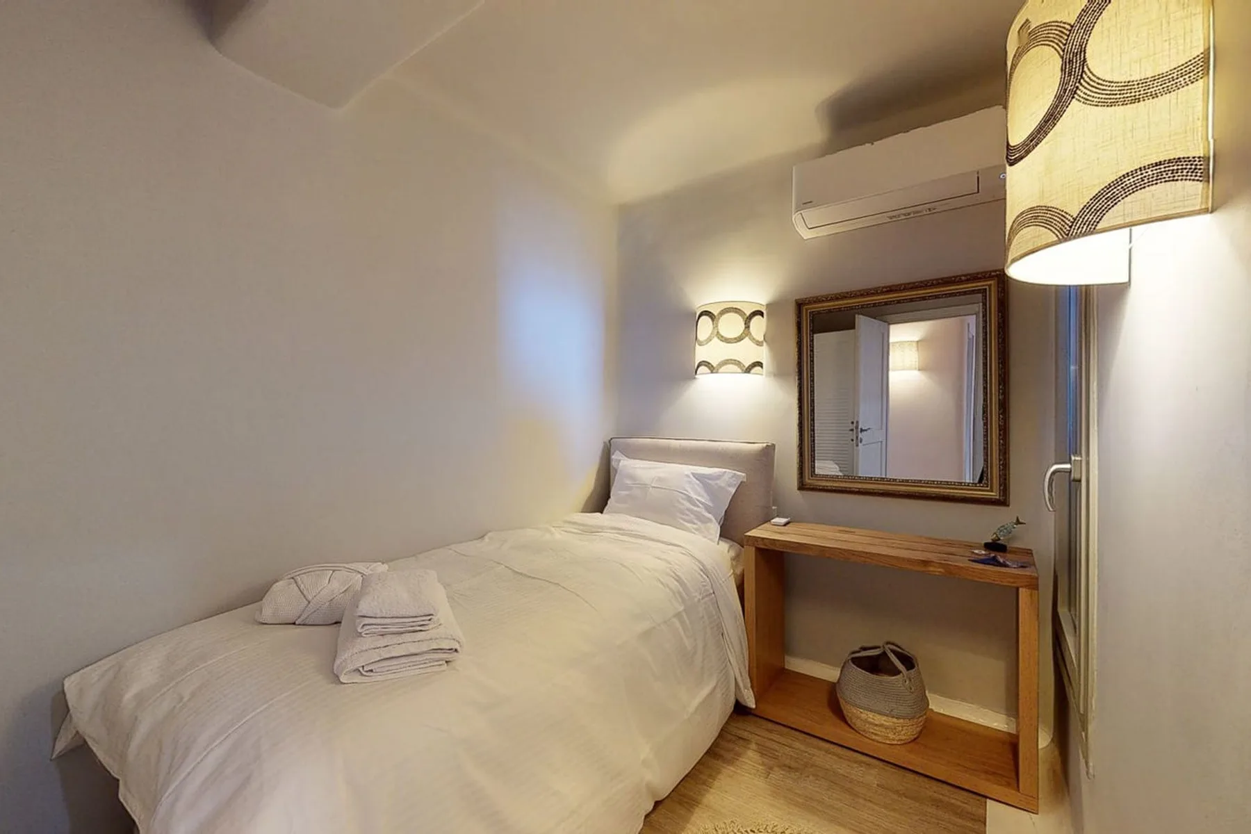 A bedroom with a neatly made bed beside a wooden desk and mirror.
